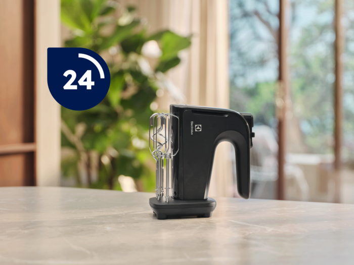 Fekete Electrolux kézi mixer márvány felületen. Kék kör "24"-gyel felette. Háttér: zöld lombozat és ablak.