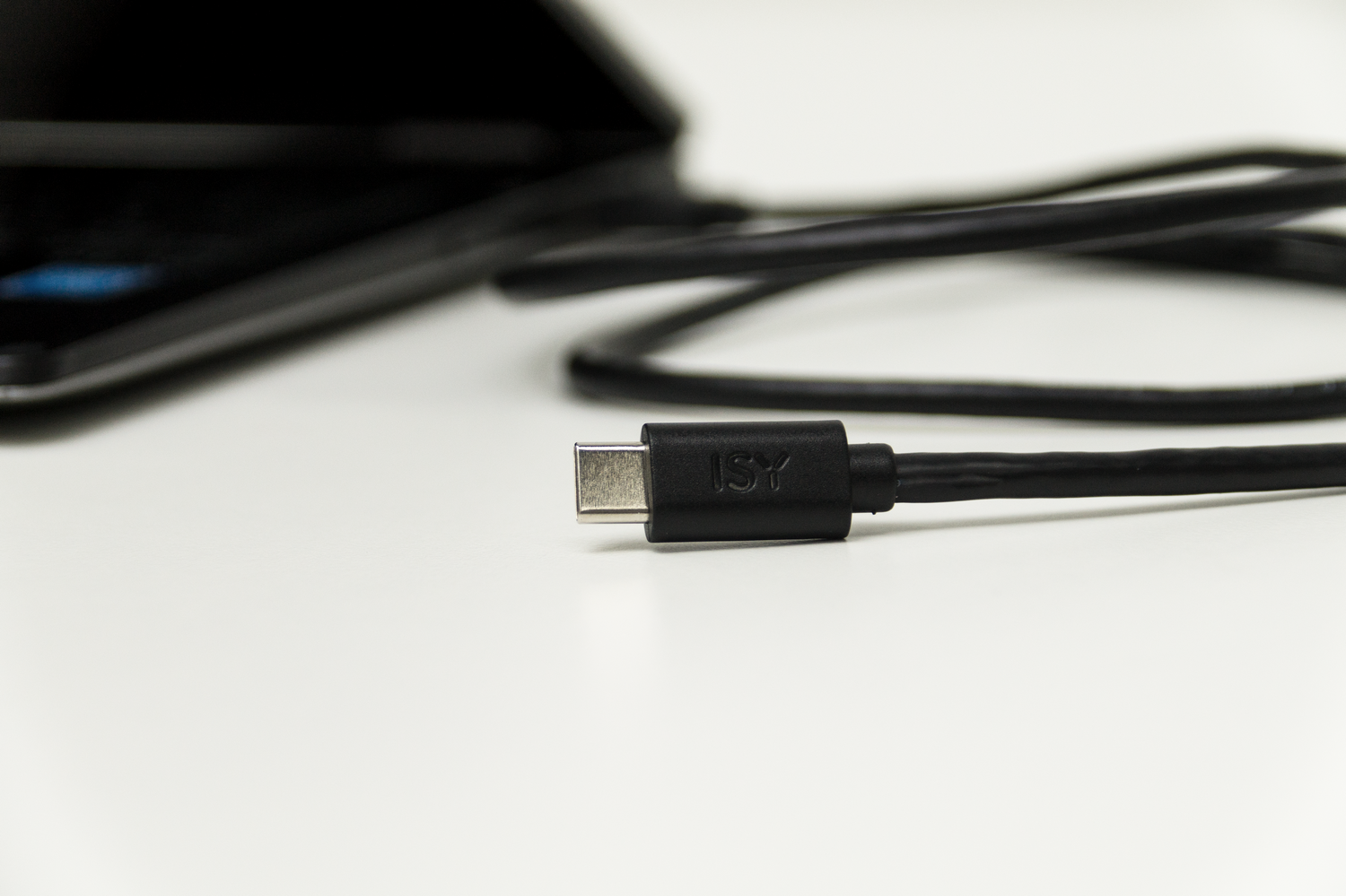 Un cable y conector USB-C negro sobre una superficie blanca, primer plano.