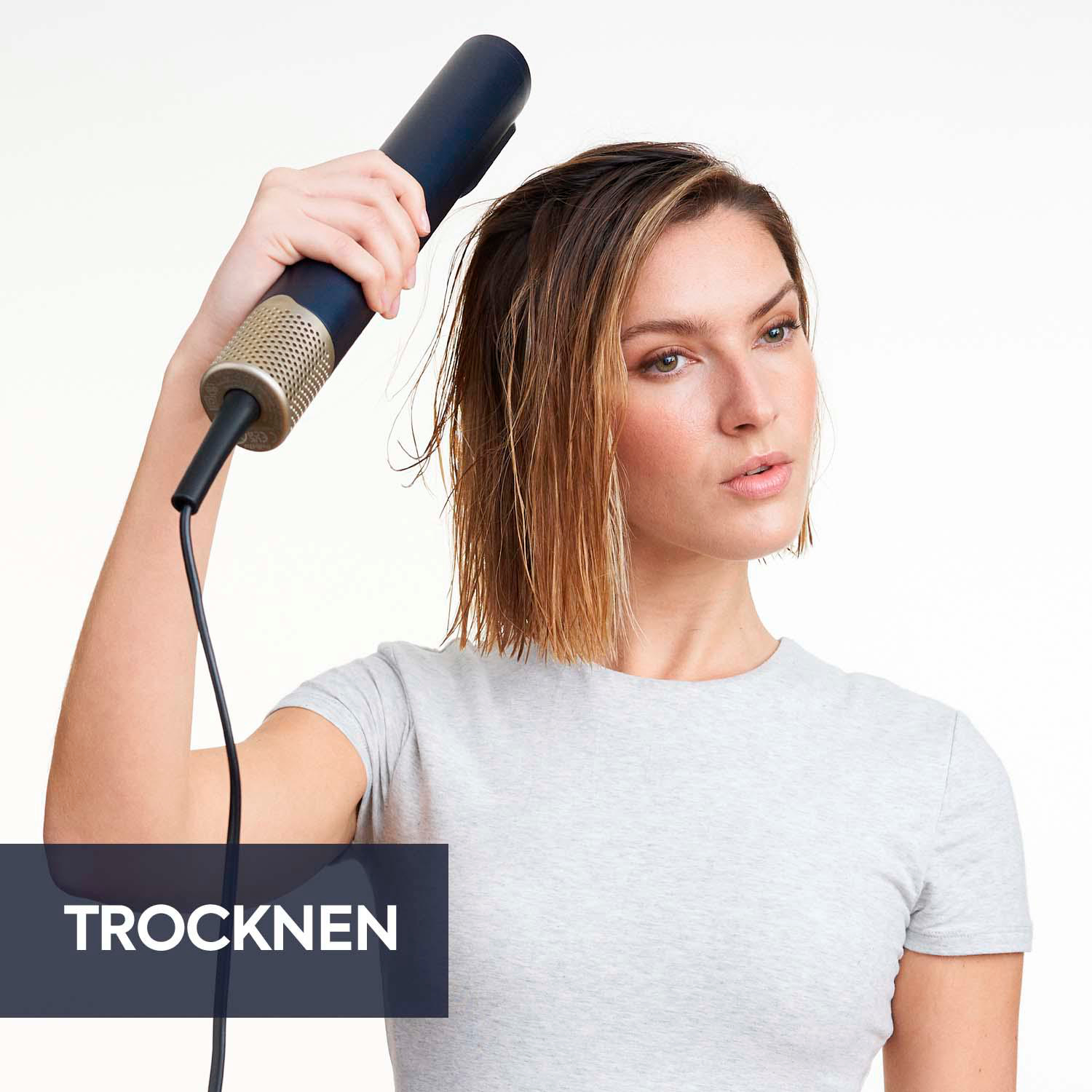 Eine Frau trocknet ihre Haare mit einem dunkelblauen und goldenen Haartrockner.