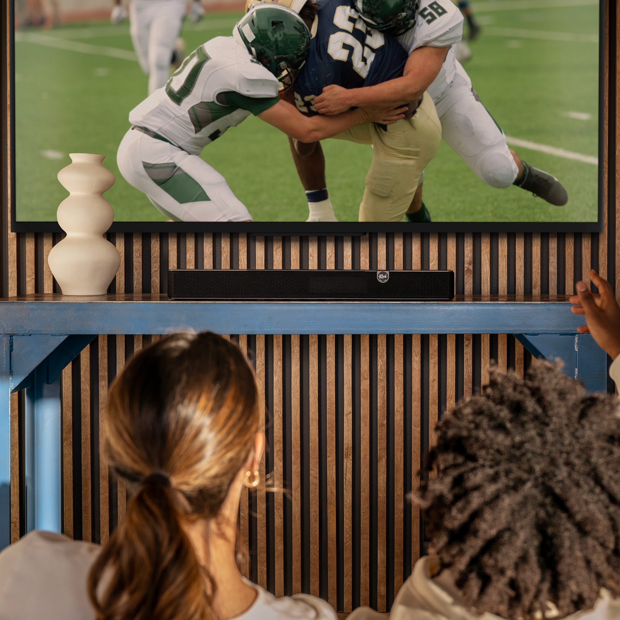 Zwei Personen schauen auf einen Fernseher, auf dem ein American-Football-Spiel läuft.