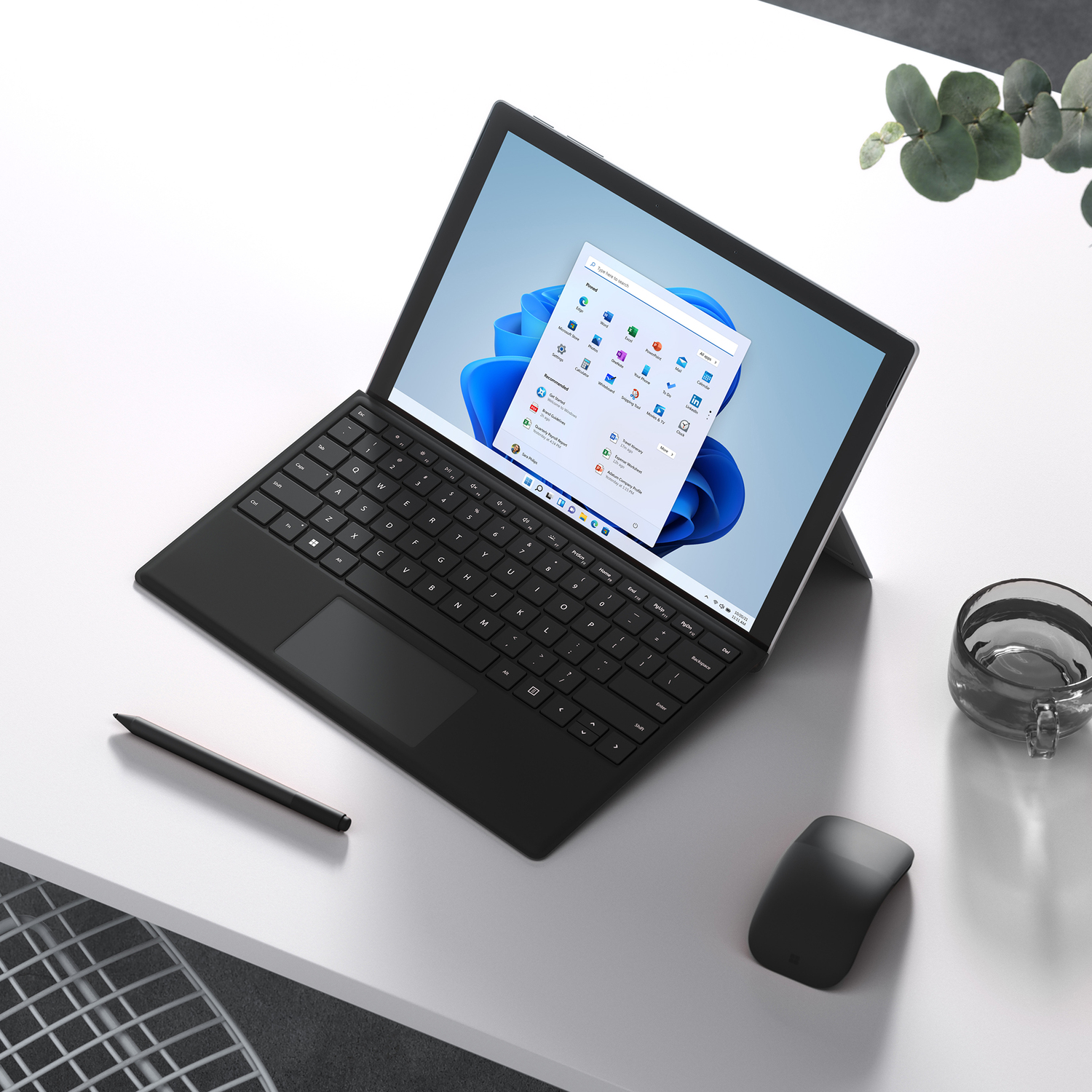 A black laptop on a white table with a mouse and stylus. Windows 11 is on the screen.