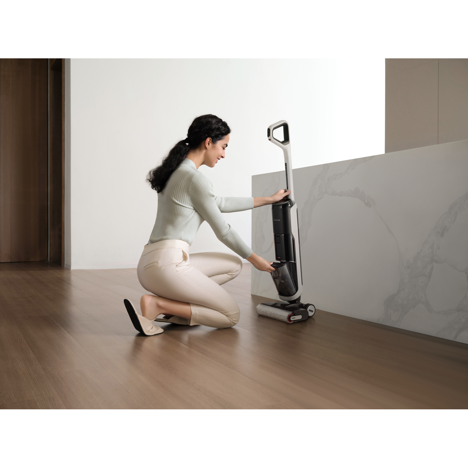 Woman using a cordless vacuum cleaner near a white countertop.