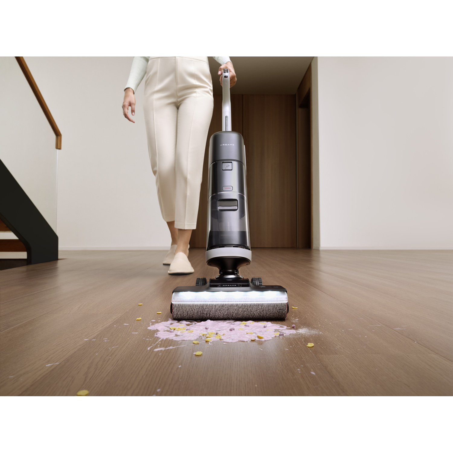 A woman uses a black and silver vacuum cleaner on a wooden floor with pink spills.
