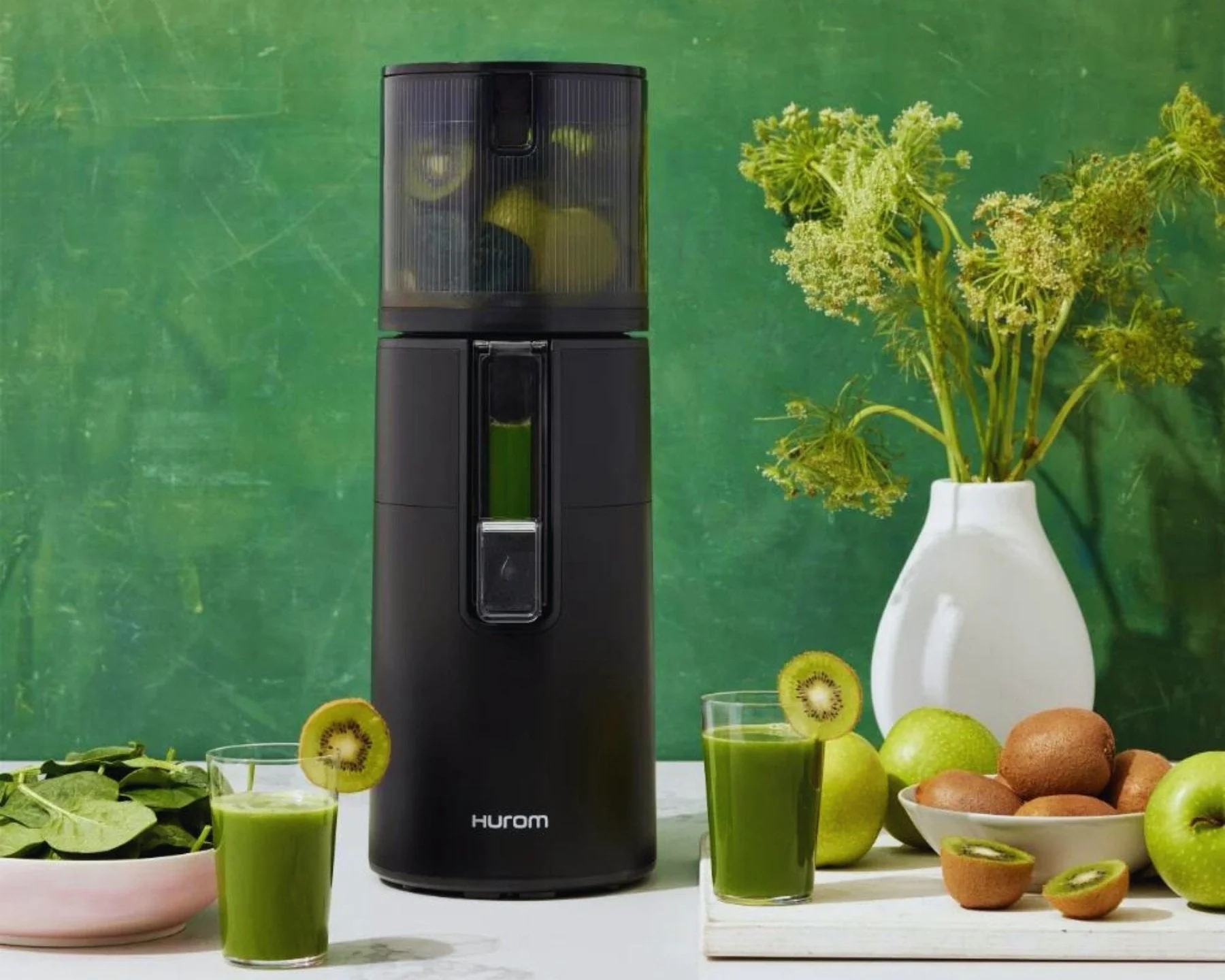 Un estrattore di succo nero, con kiwi e succo verde. Sfondo verde e bianco.