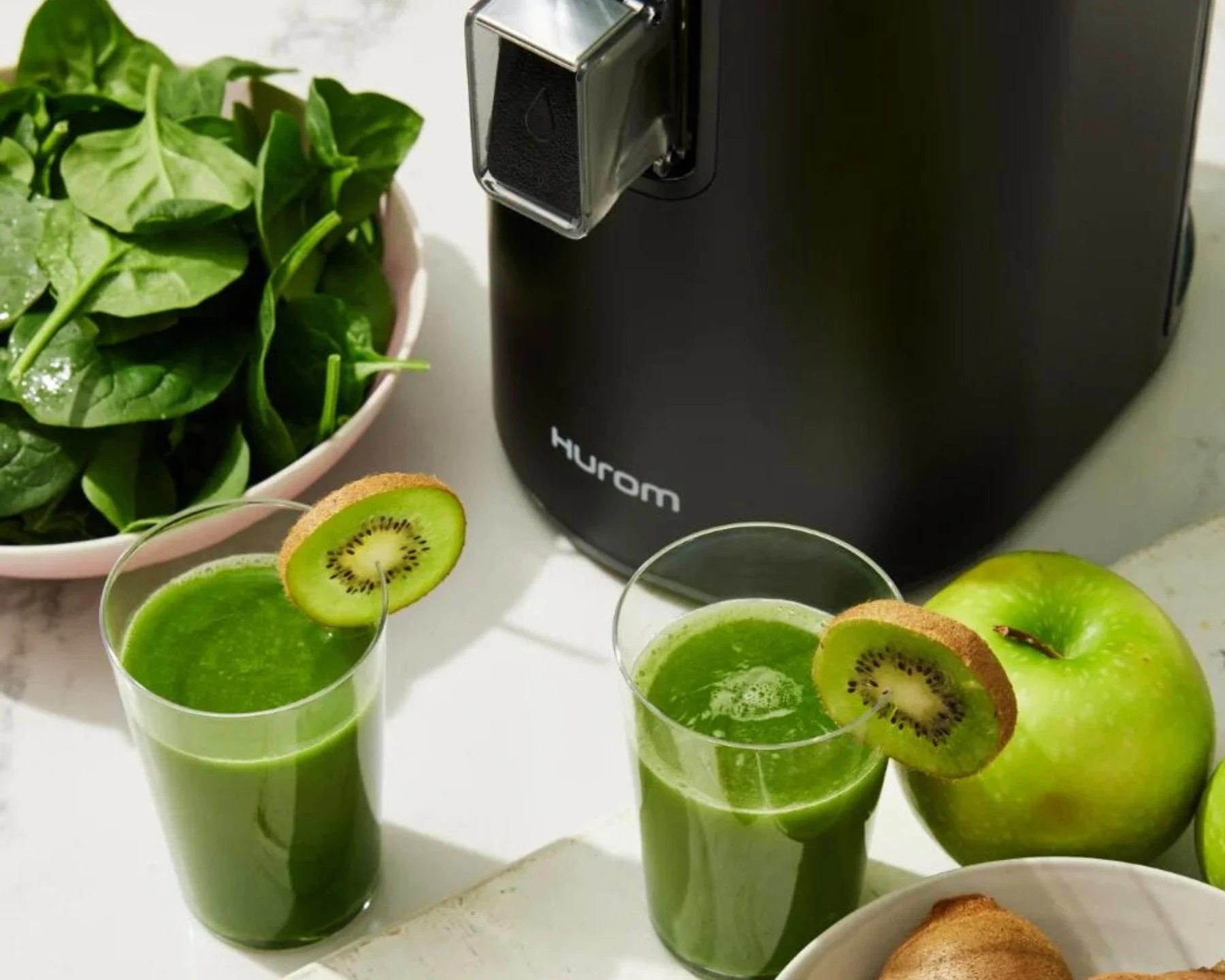 Succo verde in bicchieri con fette di kiwi, e un estrattore Hurom, con spinaci e mela.