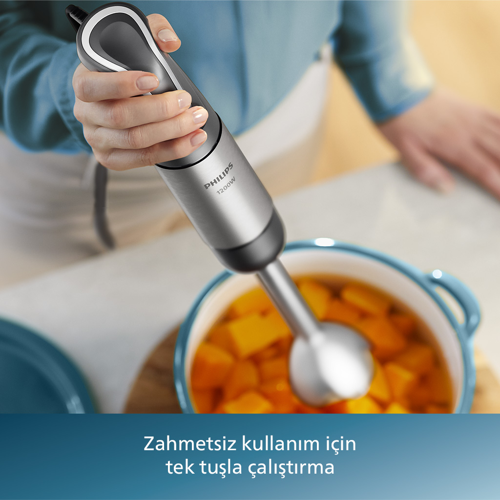 Bir kişi, balkabağı çorbası tenceresinin üzerinde gümüş bir el blenderi tutuyor.