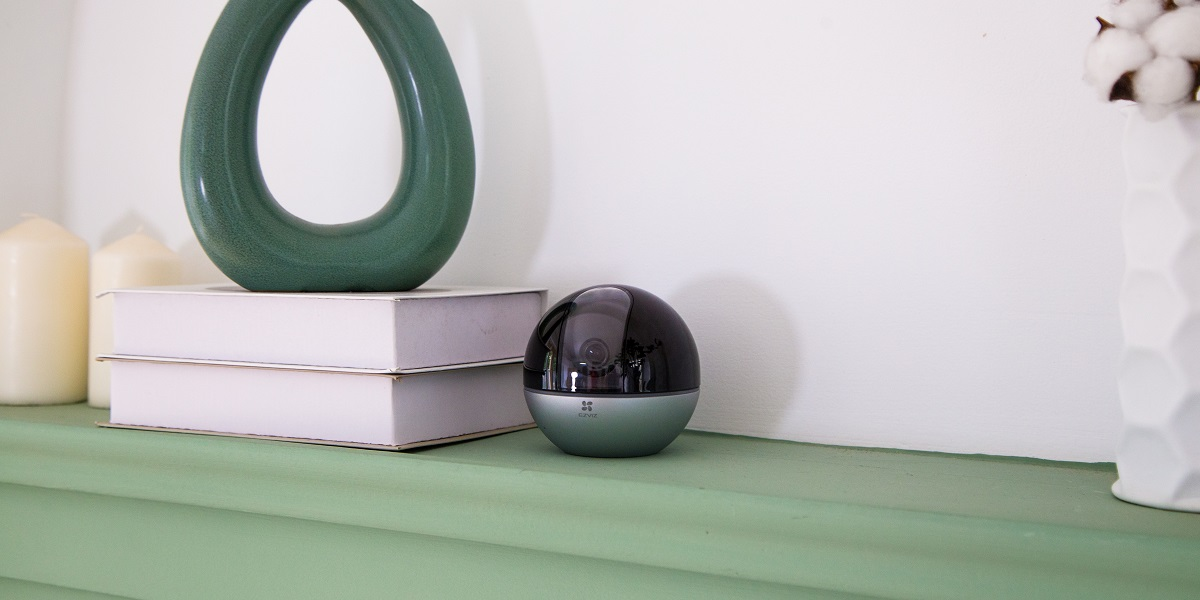 Sicherheitskamera auf mintgrüner Oberfläche. Bücher und Vase im Hintergrund.