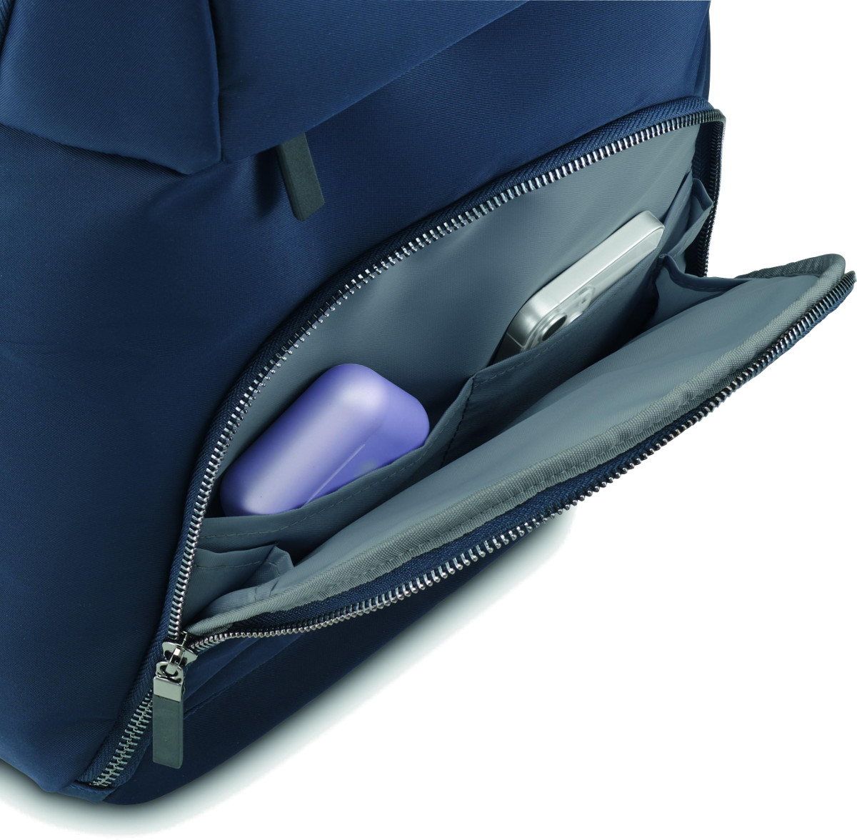 Granatowy plecak z otwartą kieszenią. W środku srebrny aparat i fioletowe mydło.