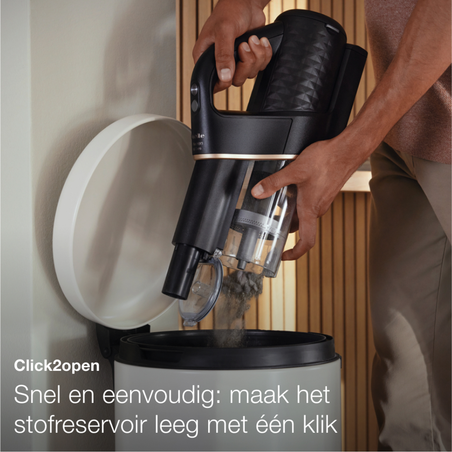 Een persoon die een zwart-gouden stofzuiger in een bak leegt.