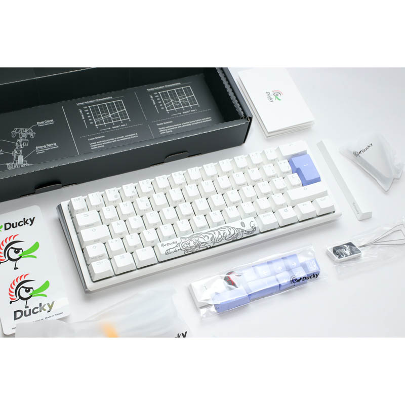 Teclado mecánico blanco con tecla azul. En la caja, con accesorios, sobre fondo blanco.