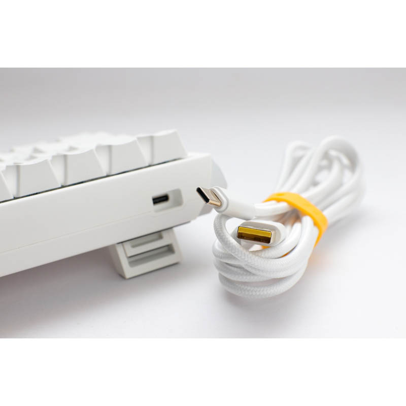 Teclado blanco con cable USB-C, enrollado y asegurado con banda amarilla.