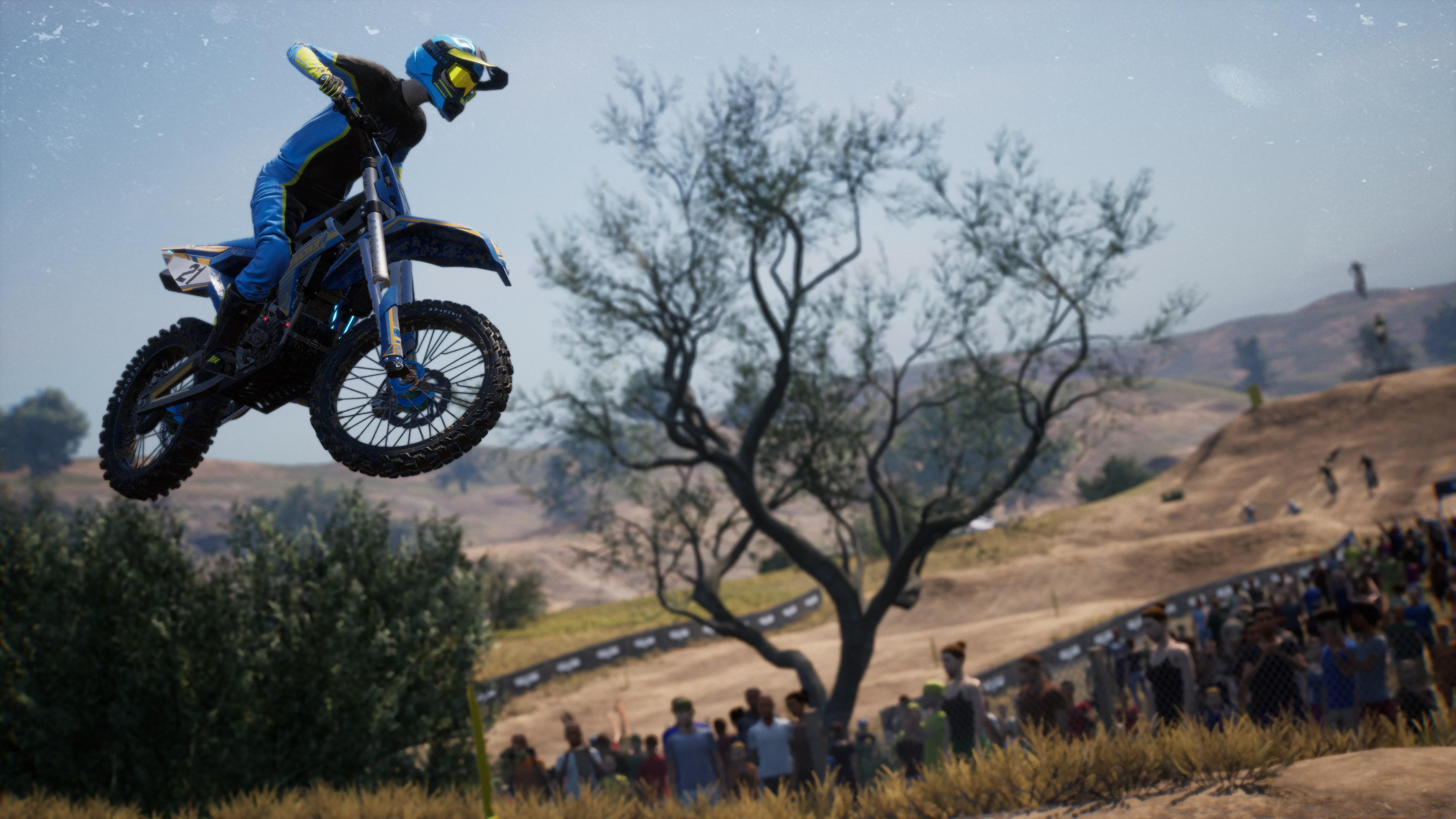 Ein Motocross-Fahrer in der Luft über einer Rennstrecke, mit Zuschauern im Hintergrund.