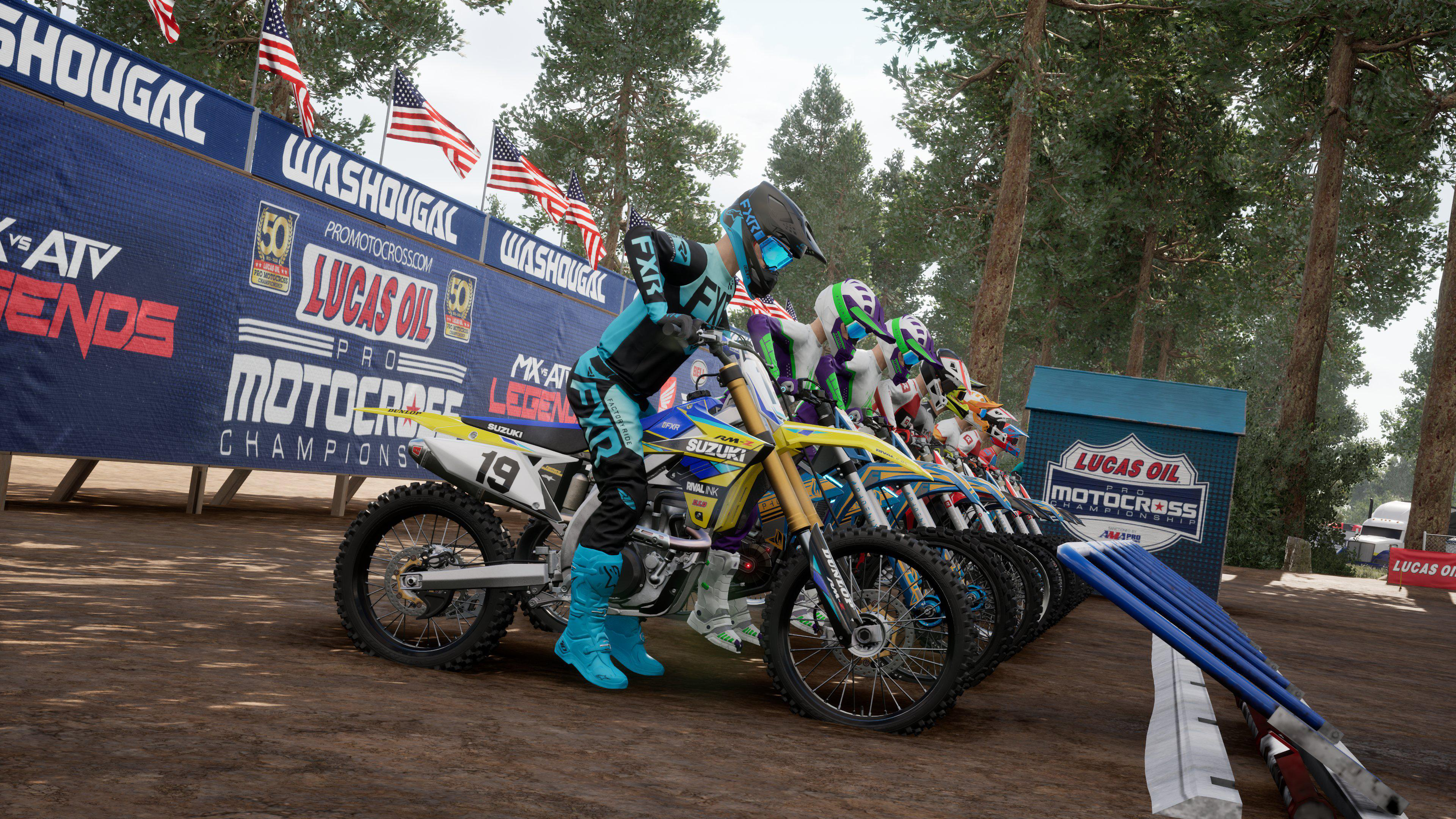 Motocross-Rennfahrer auf Motorrädern an der Startlinie eines Rennens. Flaggen und Schilder im Hintergrund.