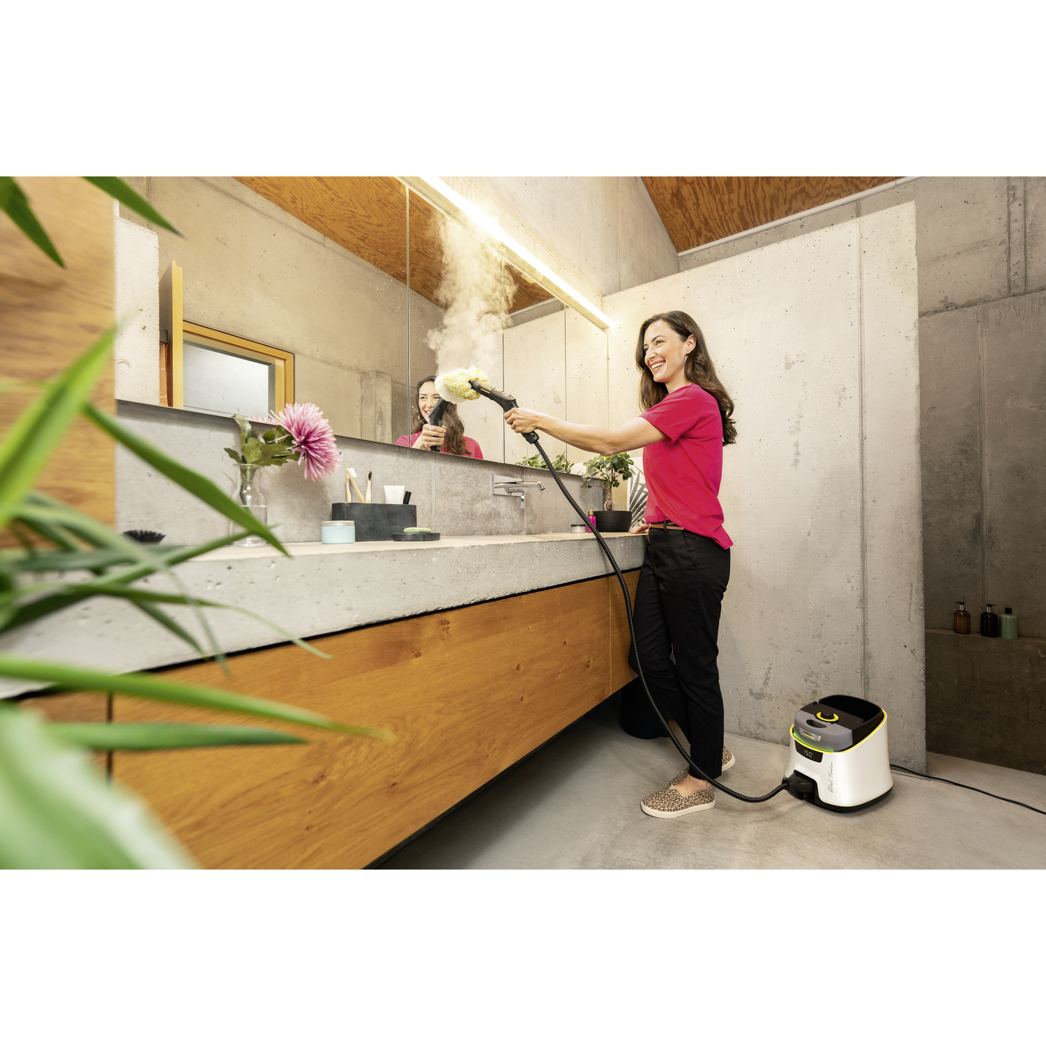Woman using a steam cleaner in a bathroom. Mirror, sink, and machine are visible.