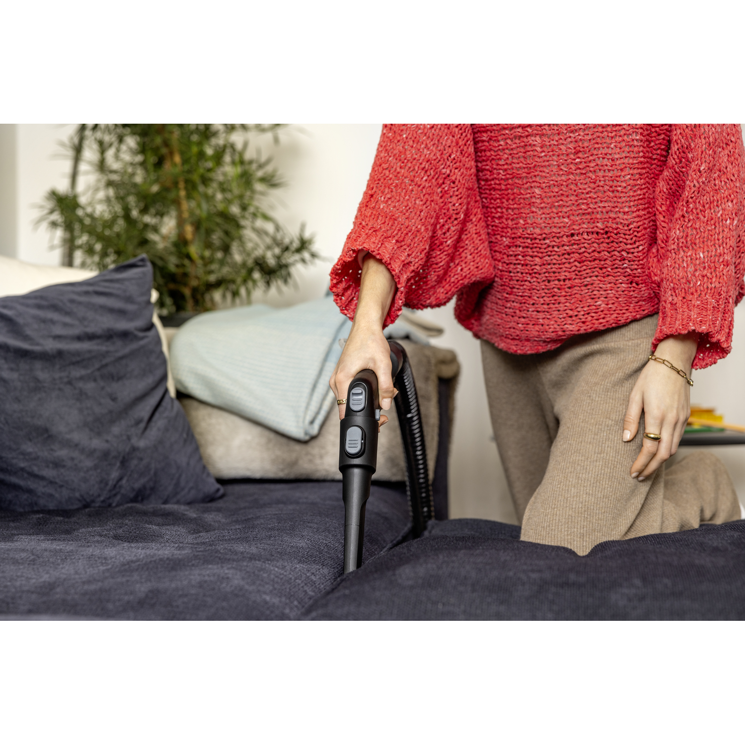 Person vacuuming a blue sofa, holding a vacuum cleaner hose with buttons visible.