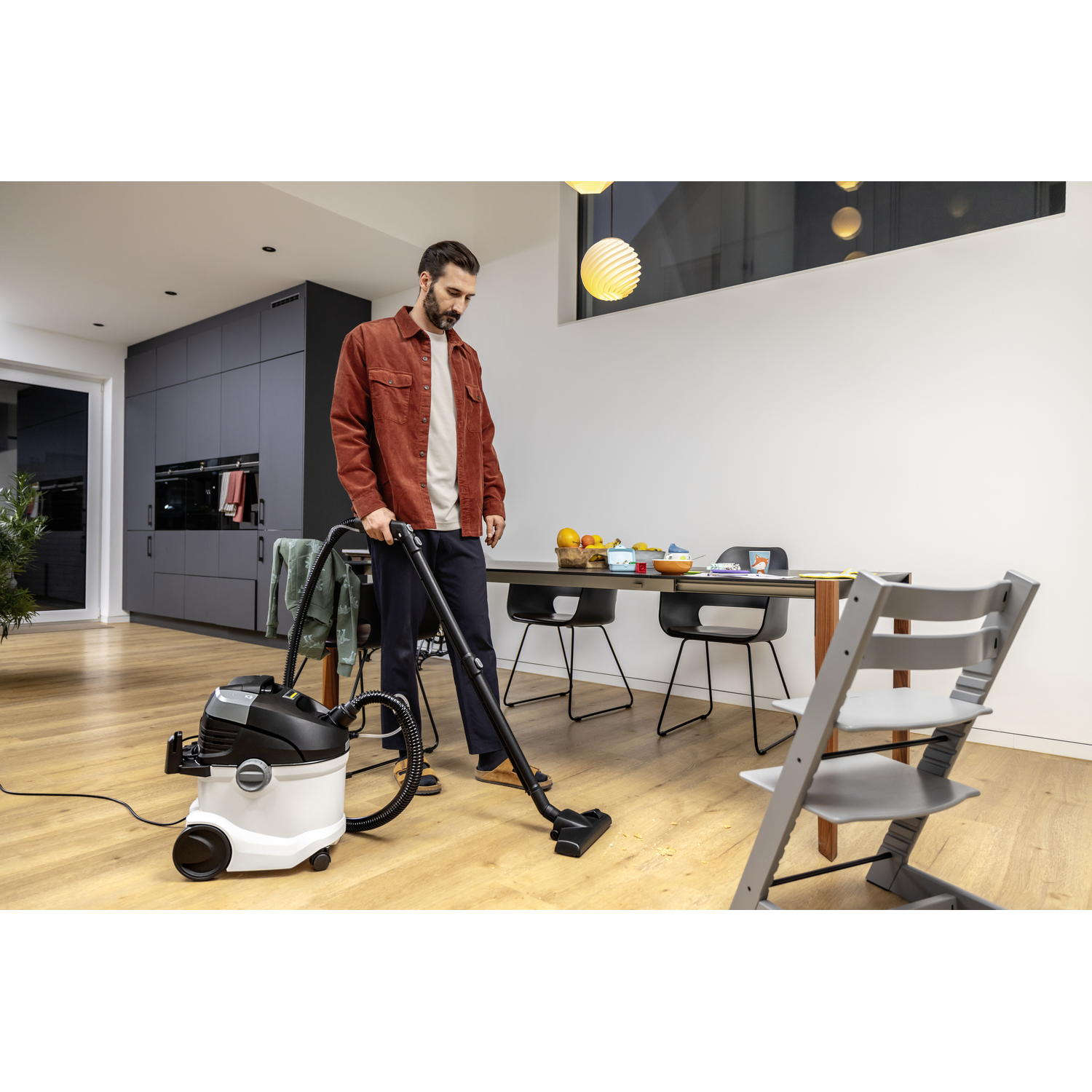 Man vacuuming a wooden floor. A dining table and chairs are in the background.