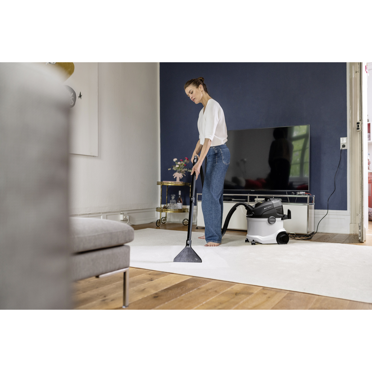 A woman cleaning a carpet with a vacuum in a living room.