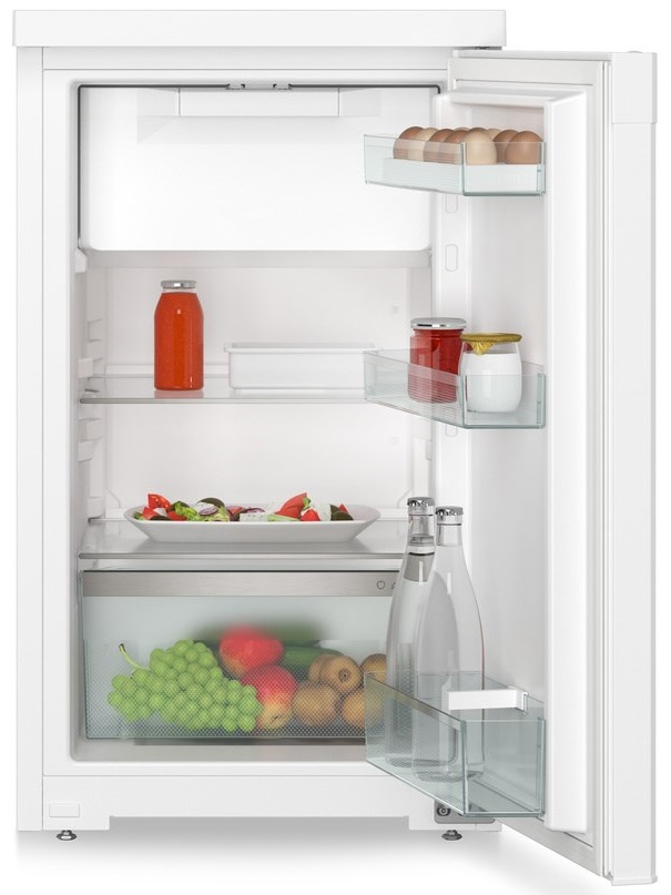 Otwarta biała lodówka z jedzeniem w środku: butelki, sałatka, owoce i słoiki.