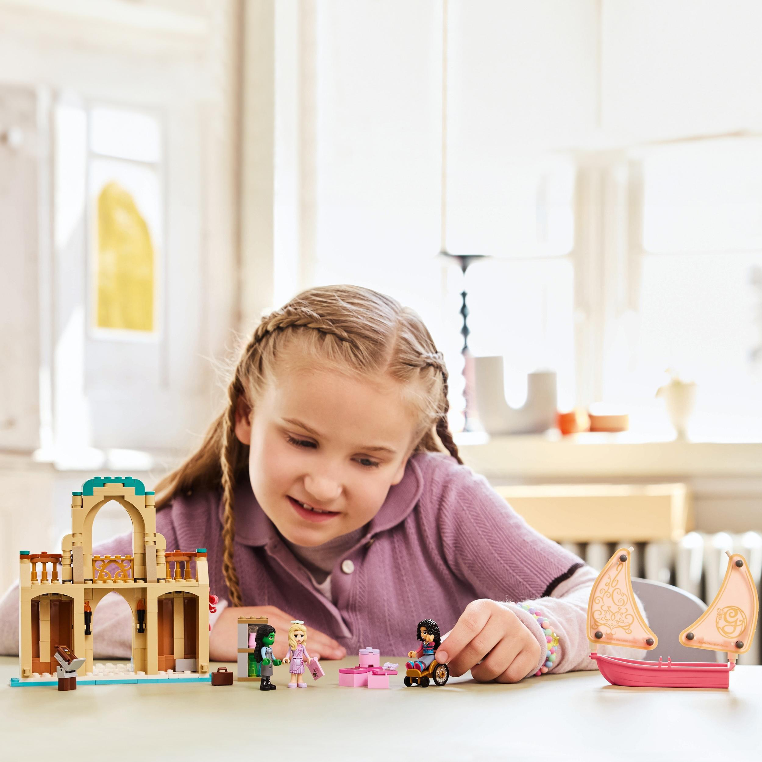 Ein Mädchen spielt mit Lego-Sets. Die Sets umfassen ein Gebäude, Figuren und ein rosa Boot.