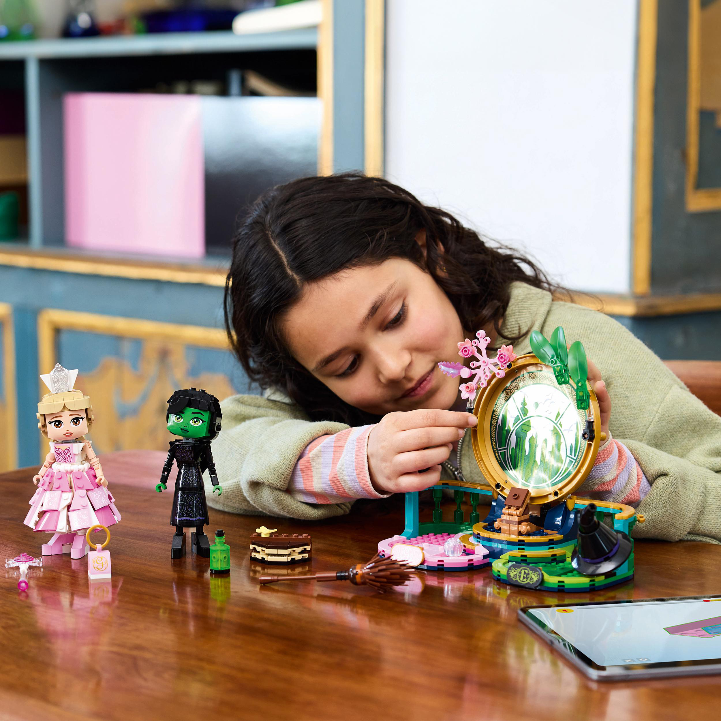 Ein Mädchen betrachtet ein Lego-Set mit Figuren und einem Spiegel. Ein Schreibtisch mit Lego-Teilen und Anleitungen ist im Vordergrund.