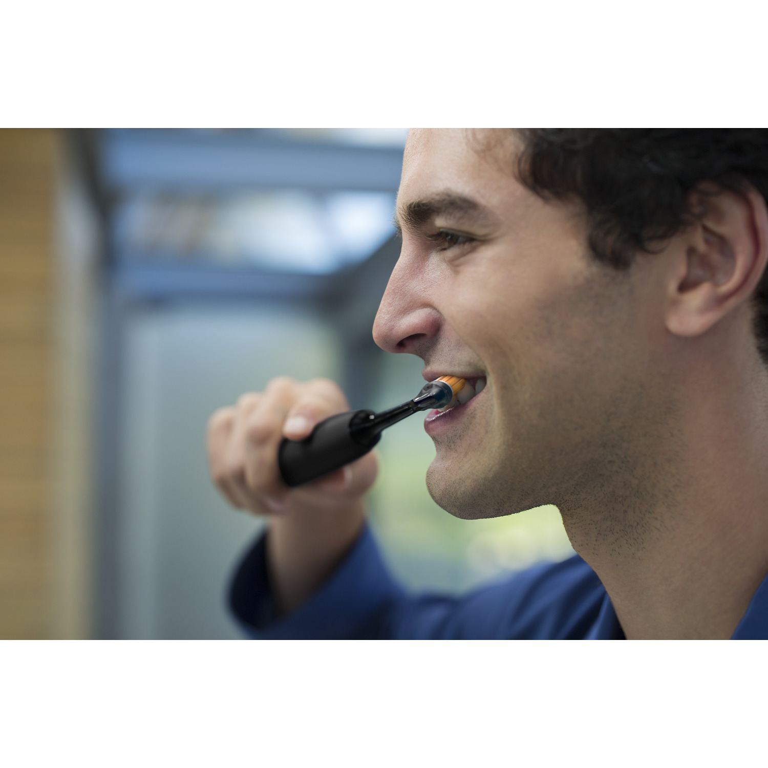 Homme se brossant les dents avec une brosse à dents électrique noire, soies oranges, en gros plan.