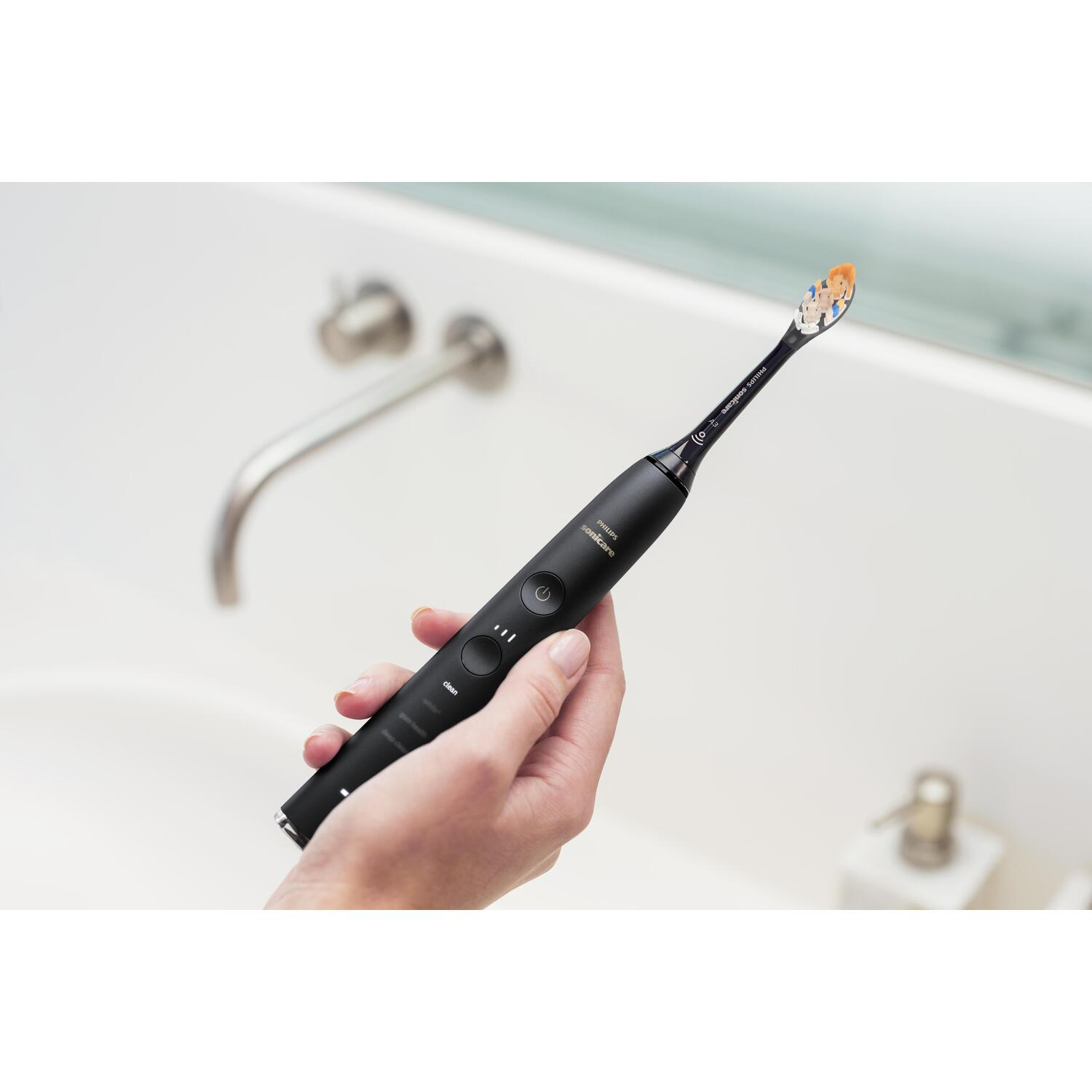 Main tenant une brosse à dents électrique noire dans une salle de bain, près d'un évier.