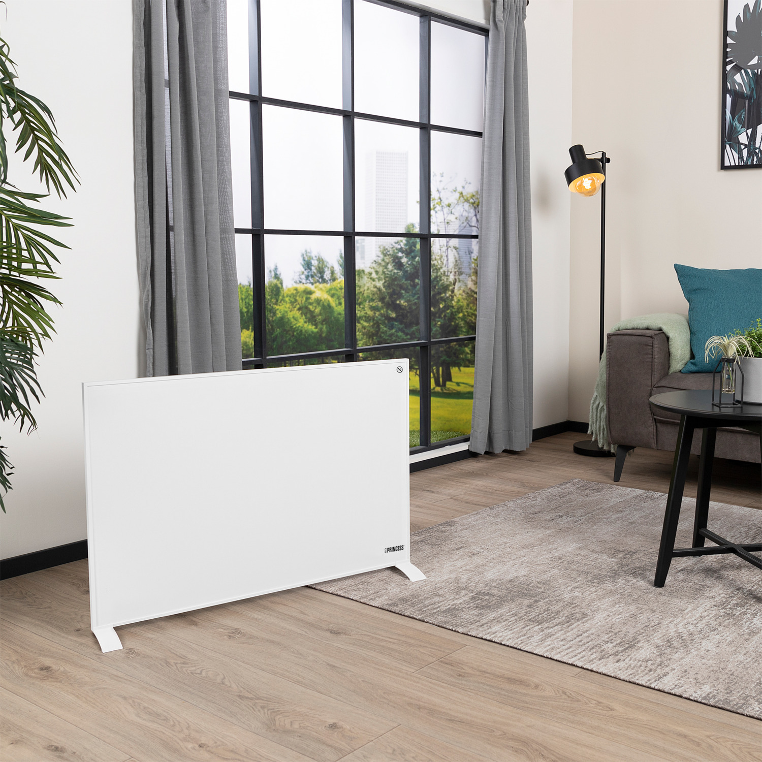 Een witte elektrische kachel in een woonkamer. Er is een raam, een bank en een tafel.