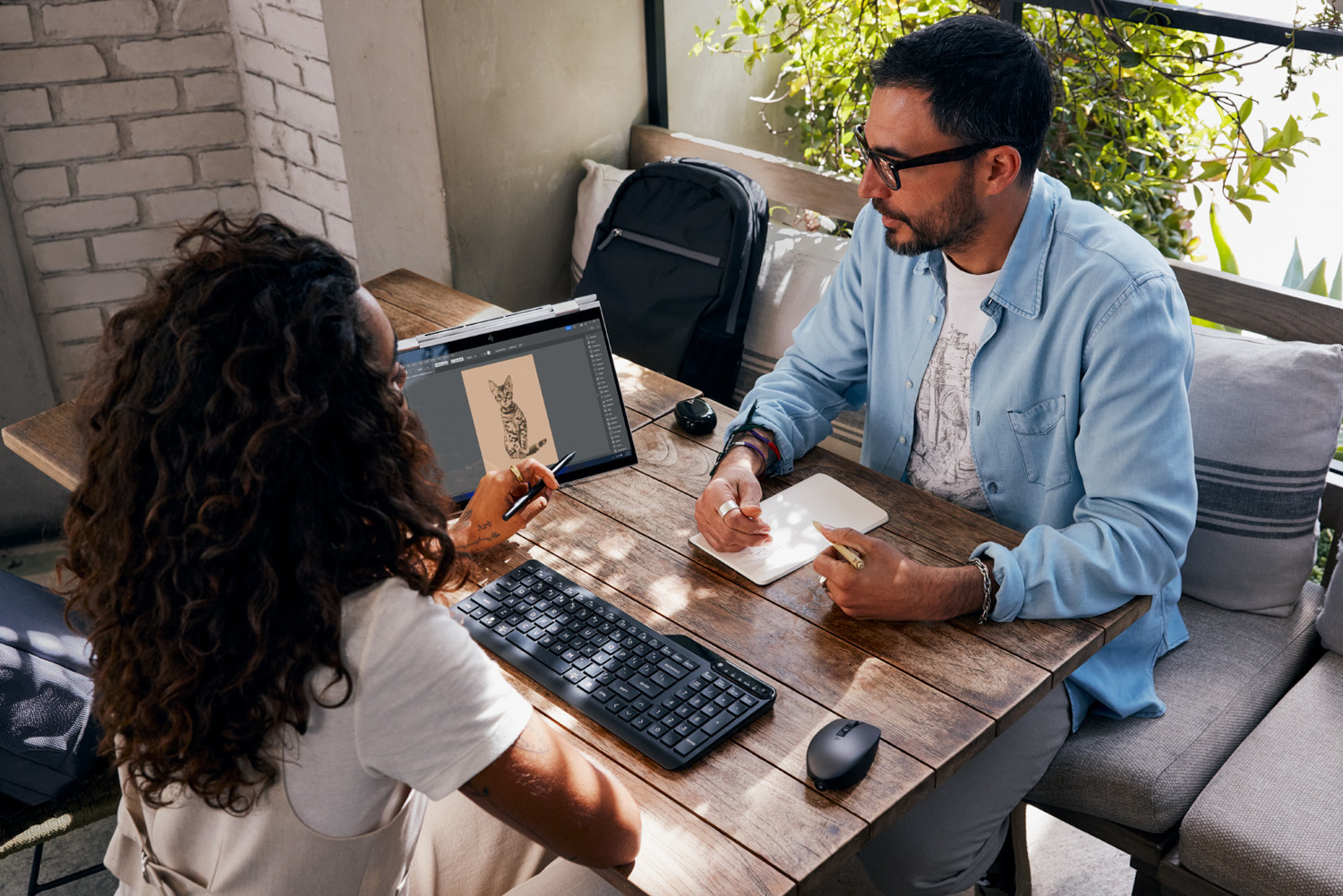 Two people at a wooden table with a laptop, keyboard, and notebook.