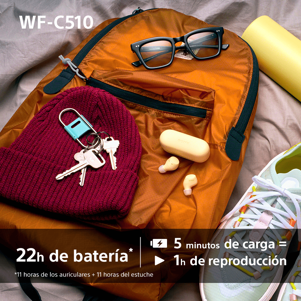 Mochila naranja con gafas, llaves, auriculares y zapatos, en una cama.