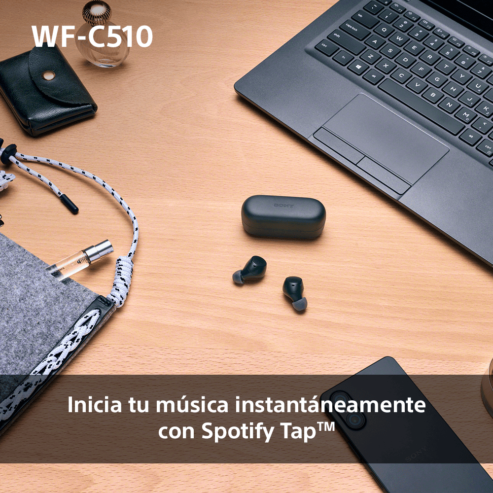 Auriculares, estuche de carga, portátil y accesorios sobre una mesa de madera.