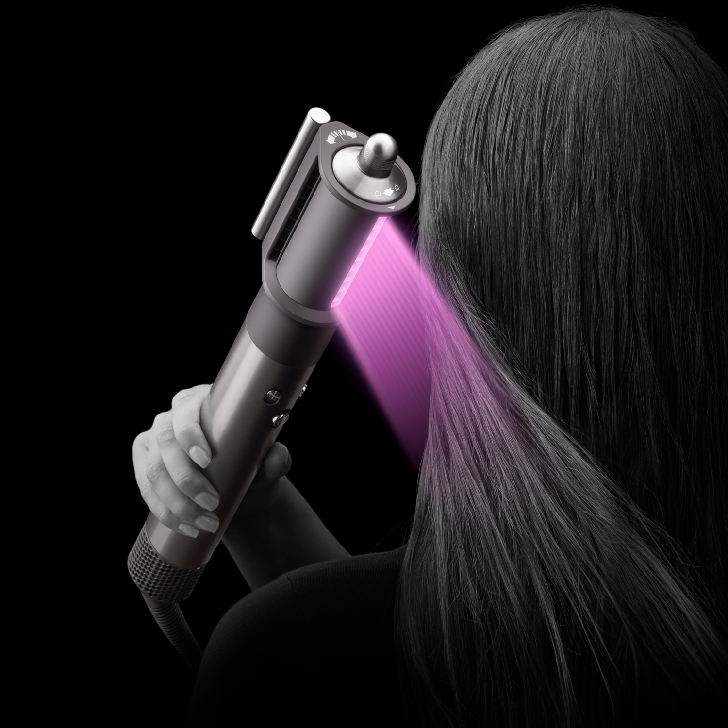 Personne tenant un styler capillaire. Lumière rose sur les cheveux. Fond noir.