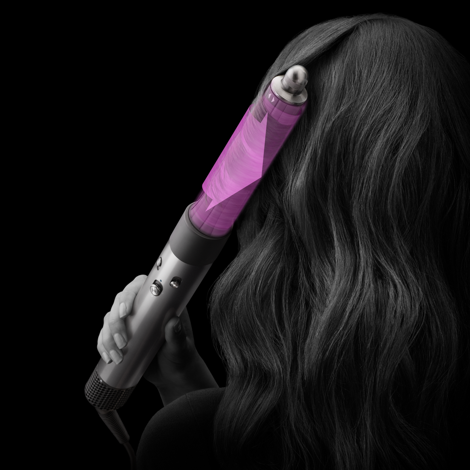 Une femme utilisant un styler à cheveux Dyson. Le styler est rose. Ses cheveux foncés sont en arrière-plan.