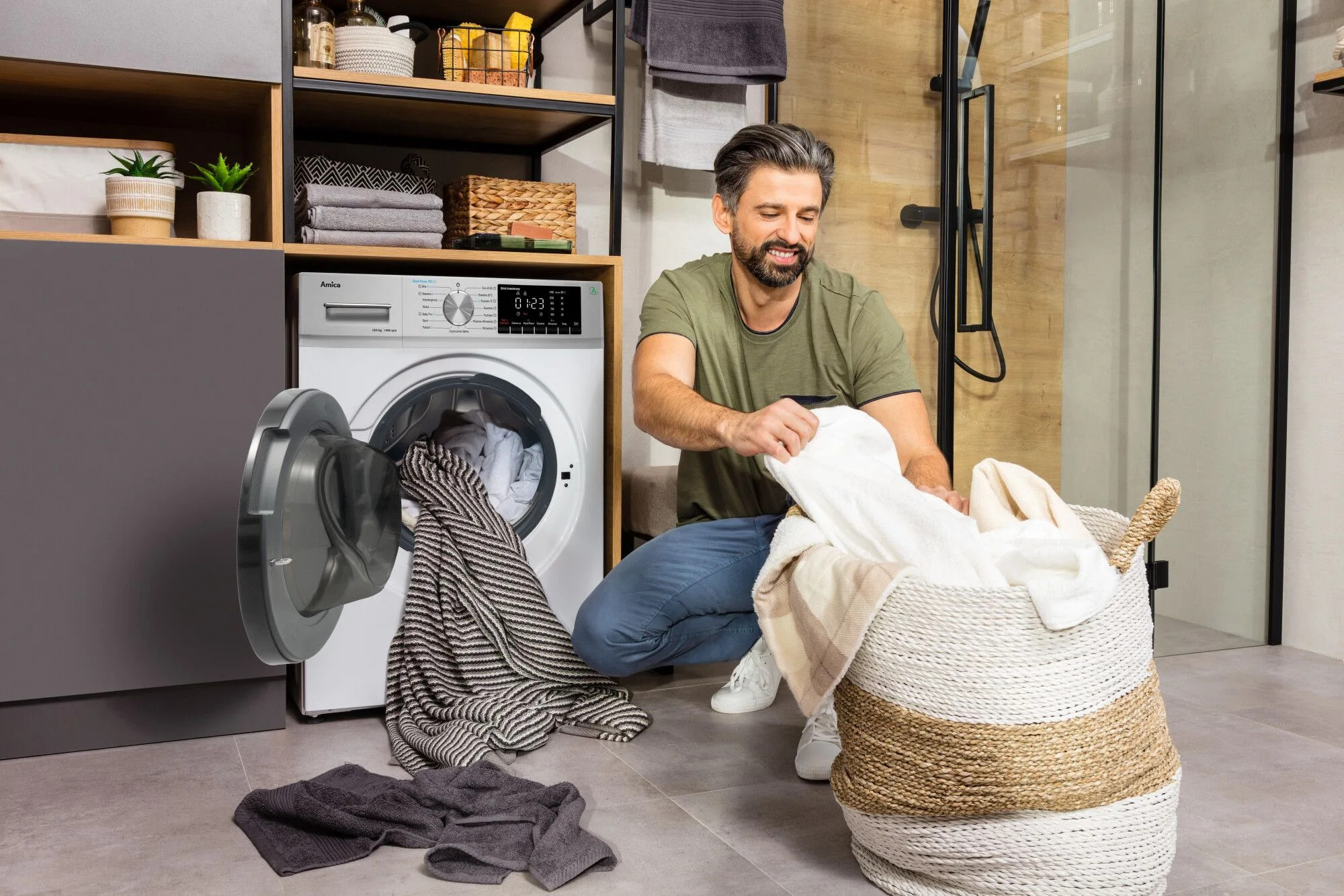 Mężczyzna wkładający pranie do pralki, obok kosz na pranie.