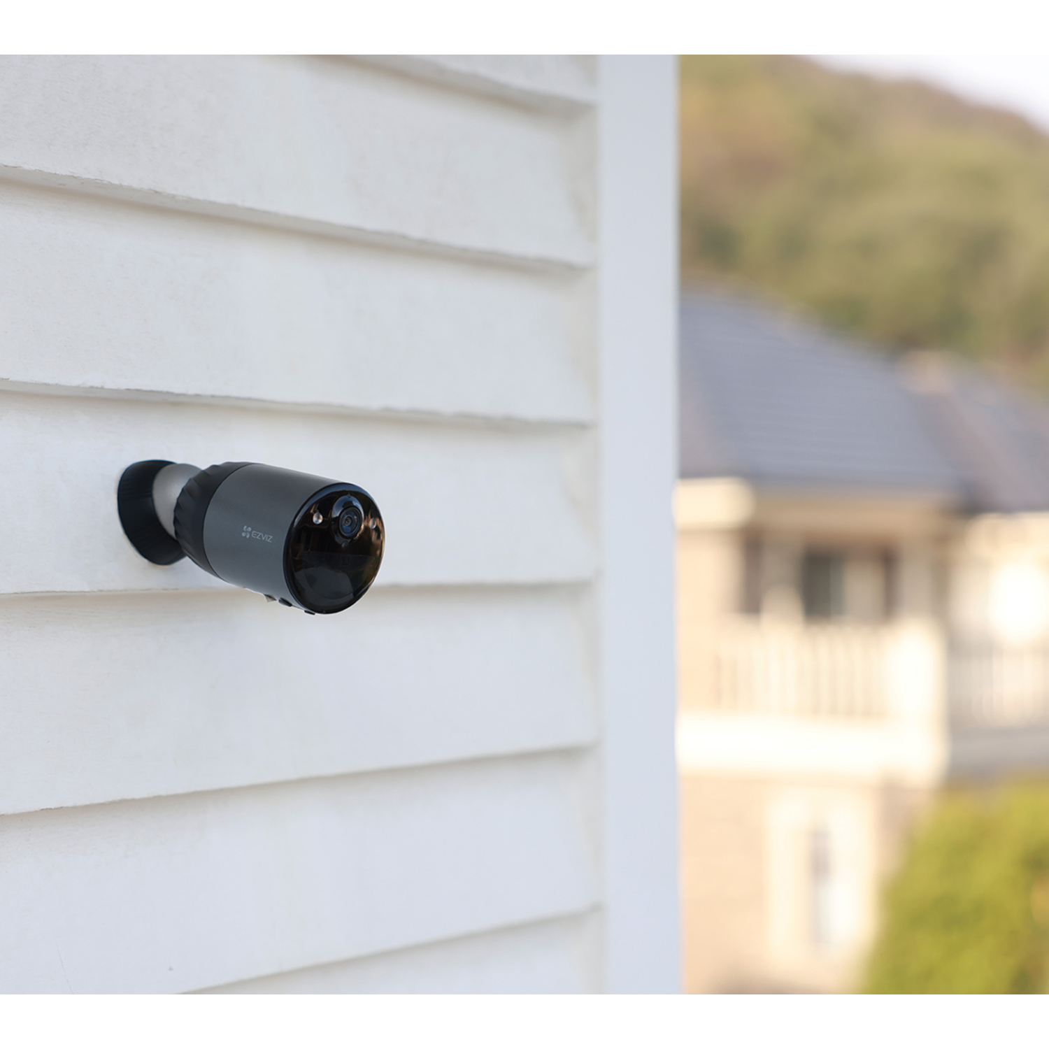 Black security camera mounted on a white wall. Blurred background of a house.
