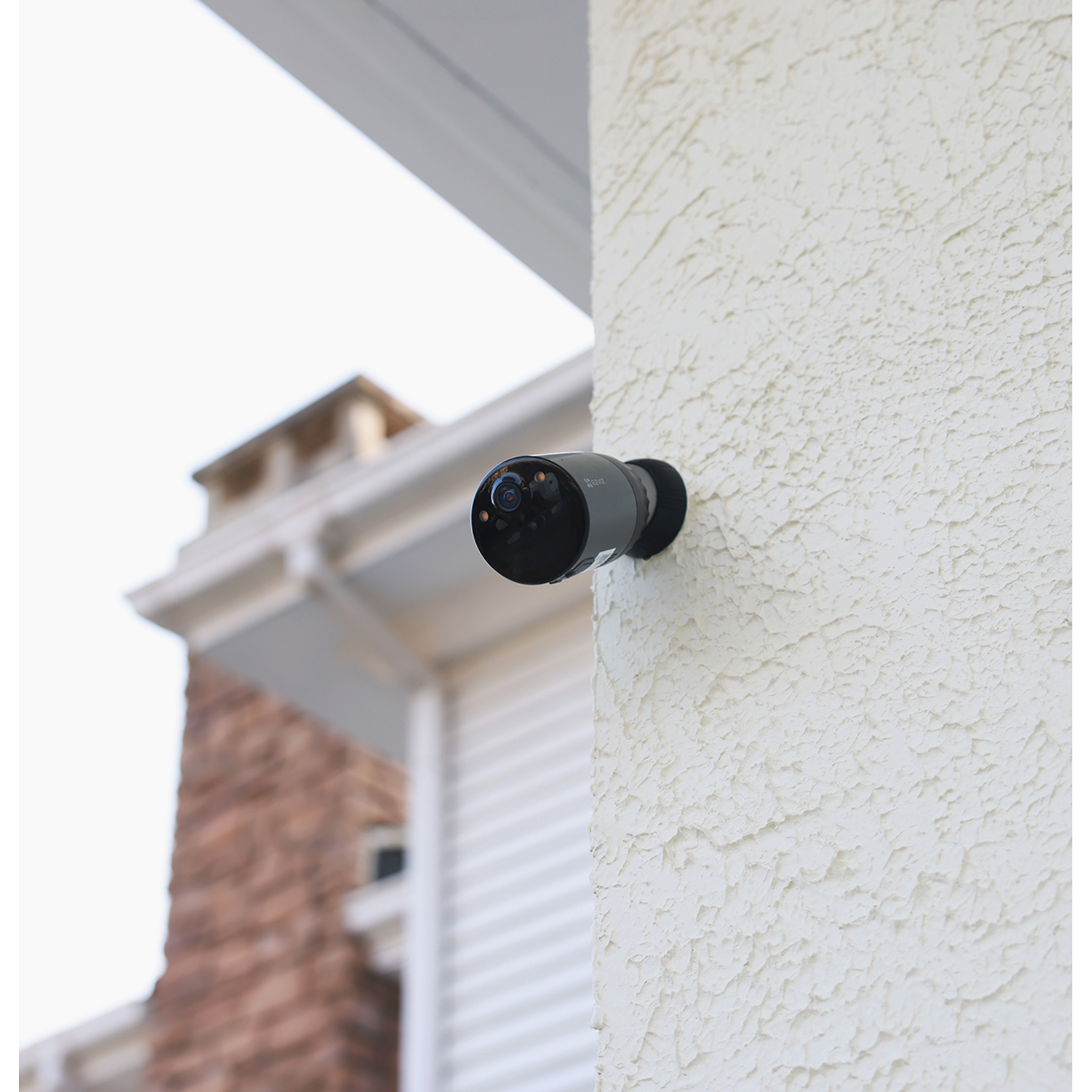 Black security camera mounted on a textured white wall, with a clear view of the lens.
