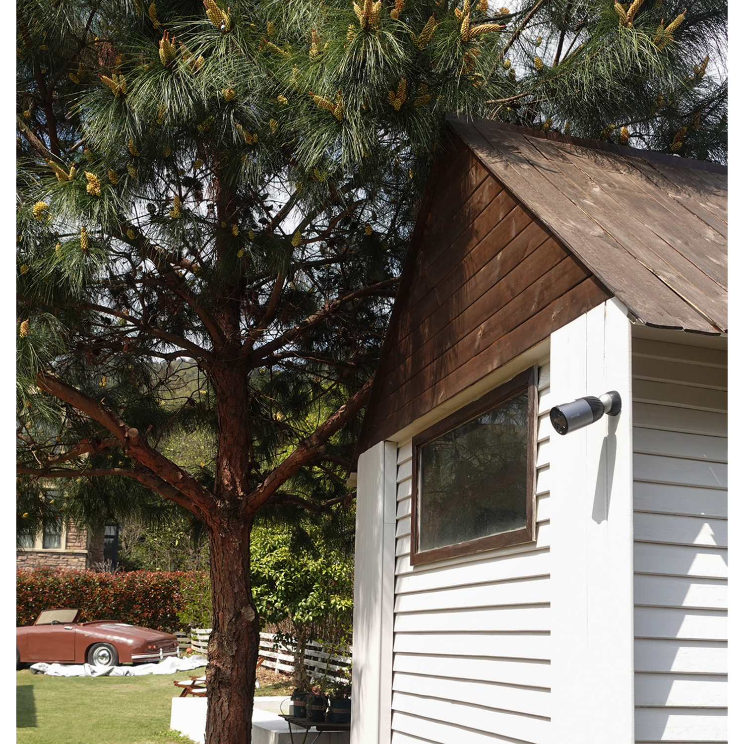 A security camera mounted on a white building near a large tree.