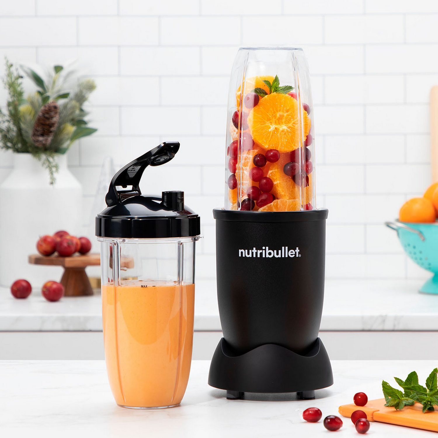Una licuadora Nutribullet negra con una taza llena al lado. Naranjas y arándanos dentro.