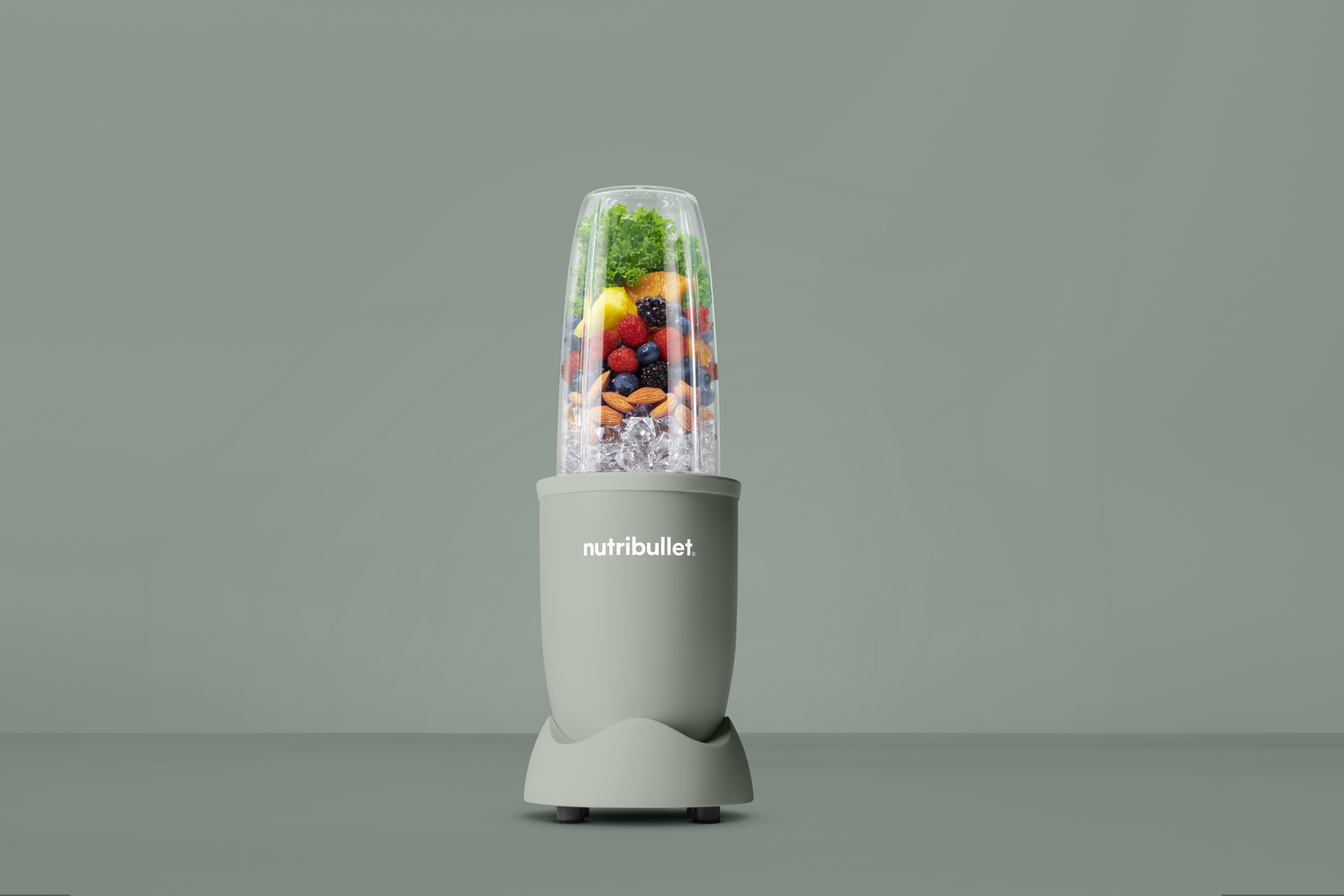 Una licuadora Nutribullet con frutas y hielo dentro, sobre un fondo verde.