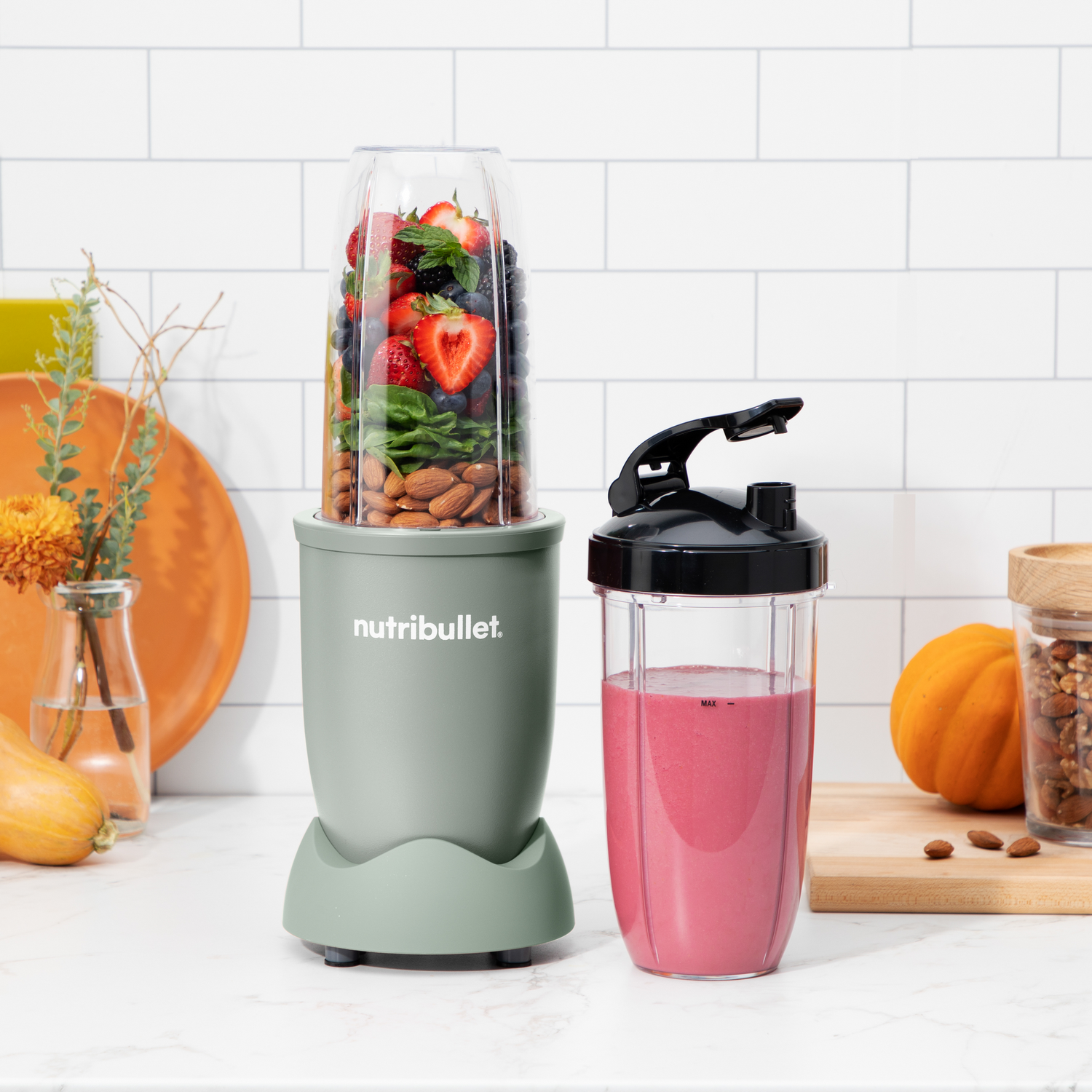 Licuadora con frutas y nueces en el recipiente y batido rosa en la taza.