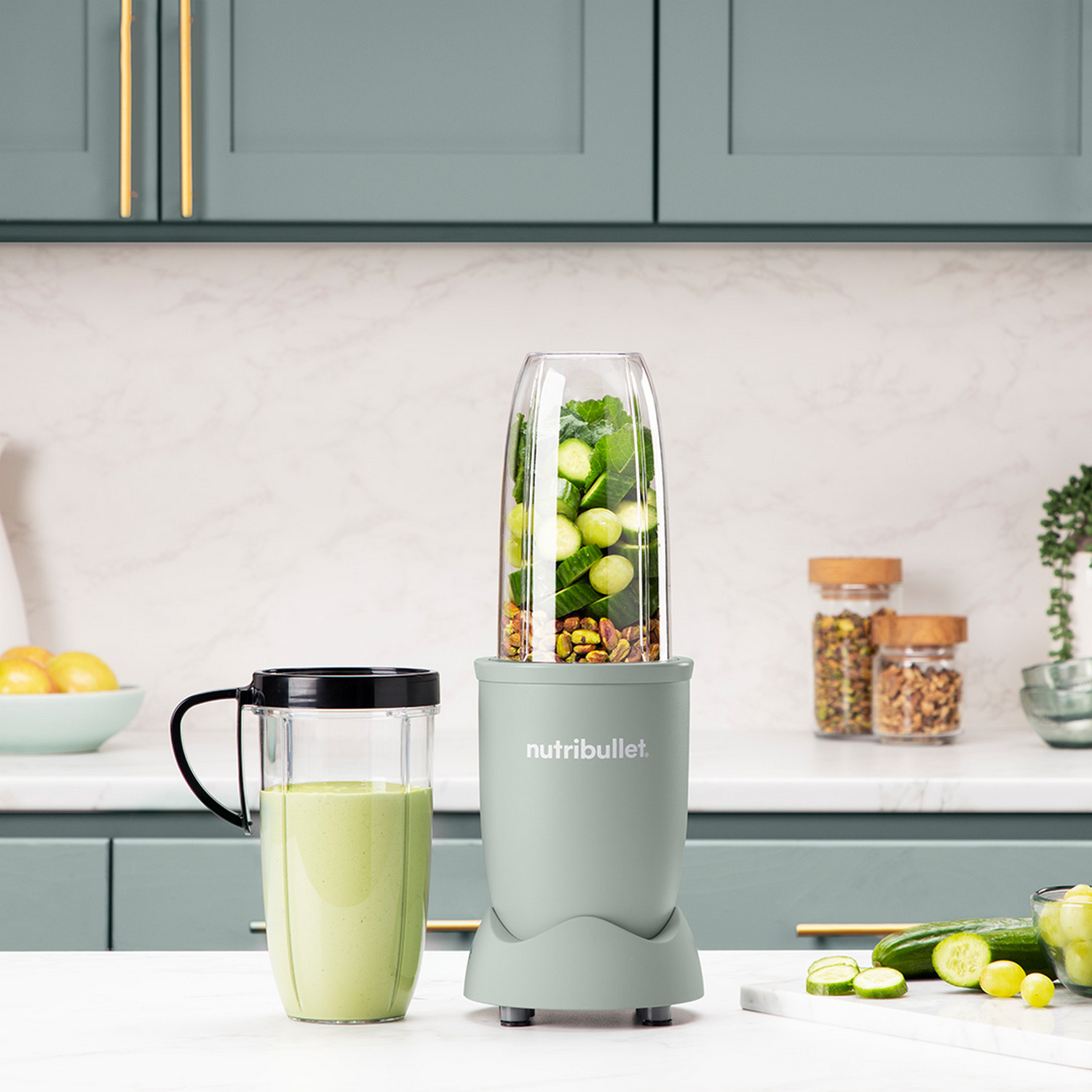 Licuadora con batido verde e ingredientes. Gabinetes verdes al fondo.