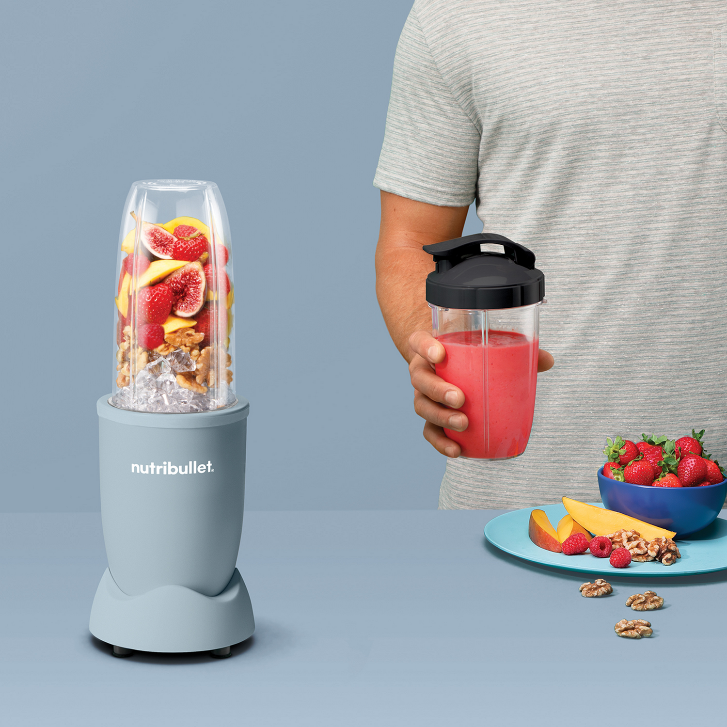 Persona usando Nutribullet. Licuadora con fruta. Fresas y fruta en plato. Batido en una taza.