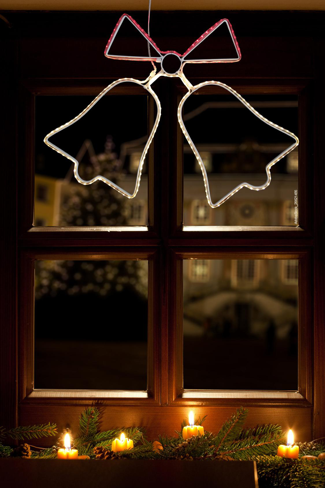 Ein Fenster mit einer Weihnachtsglockenleuchte und Kerzen auf der Fensterbank.
