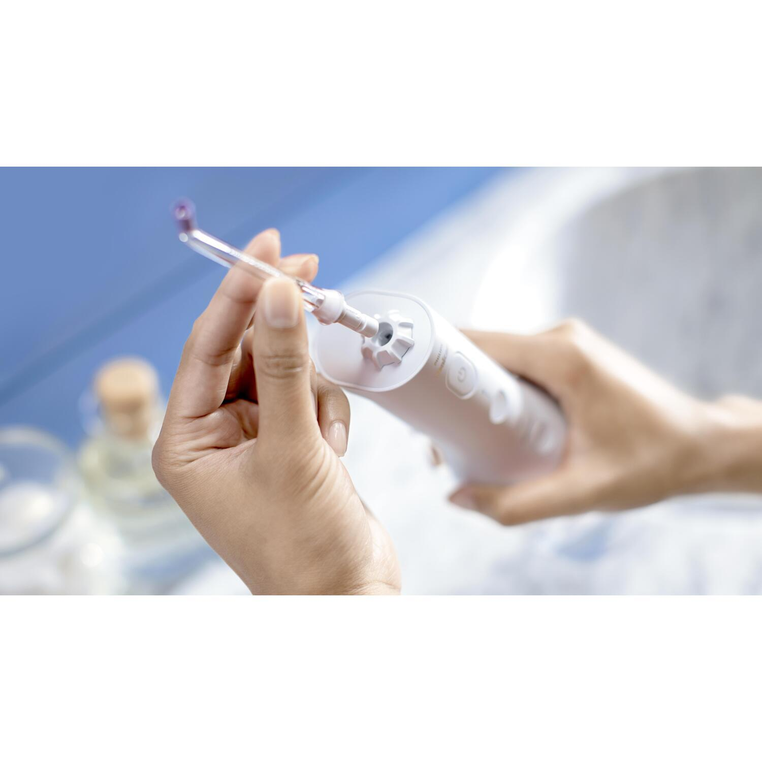 Mains tenant un hydropulseur dentaire blanc.