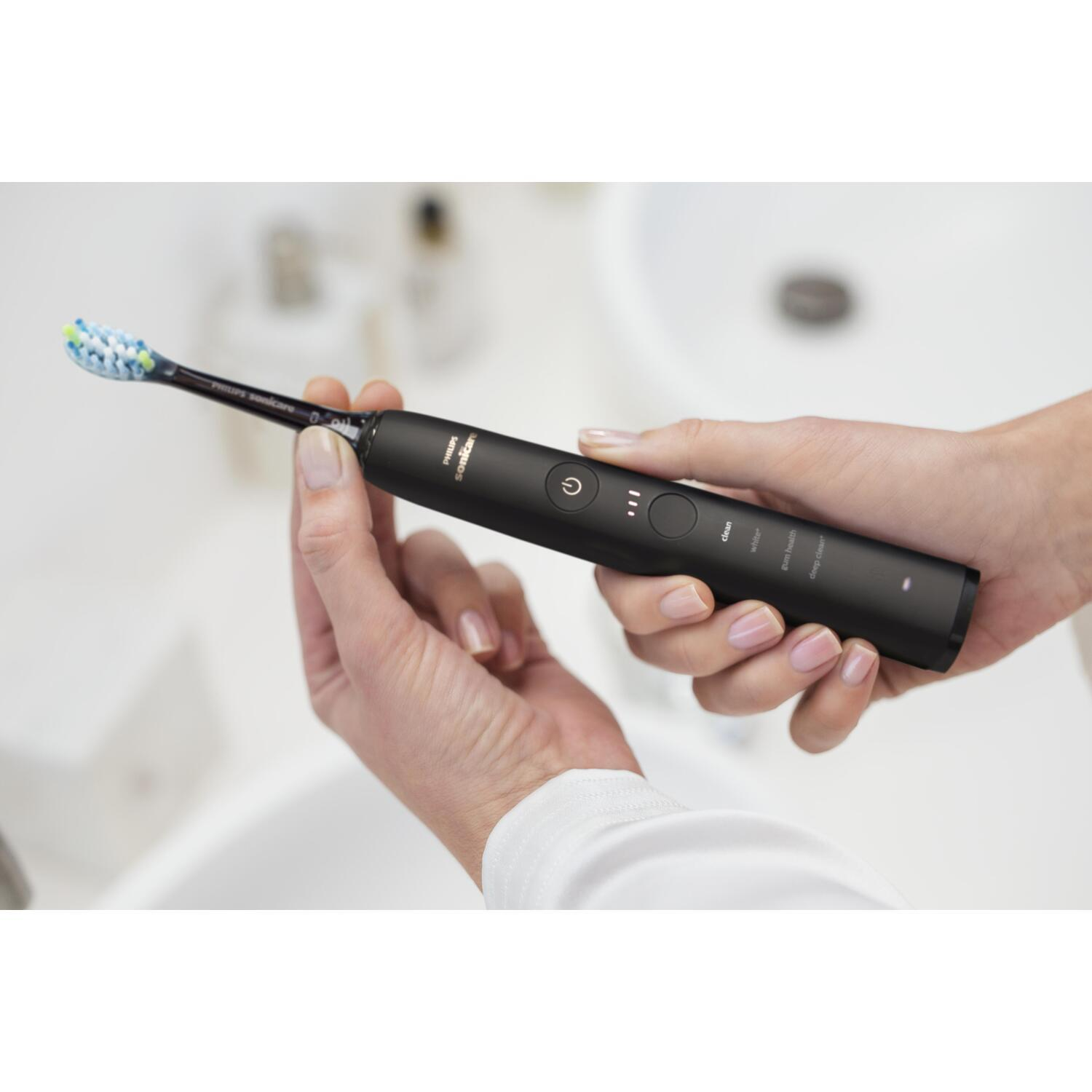 A person holding a black electric toothbrush next to a sink.