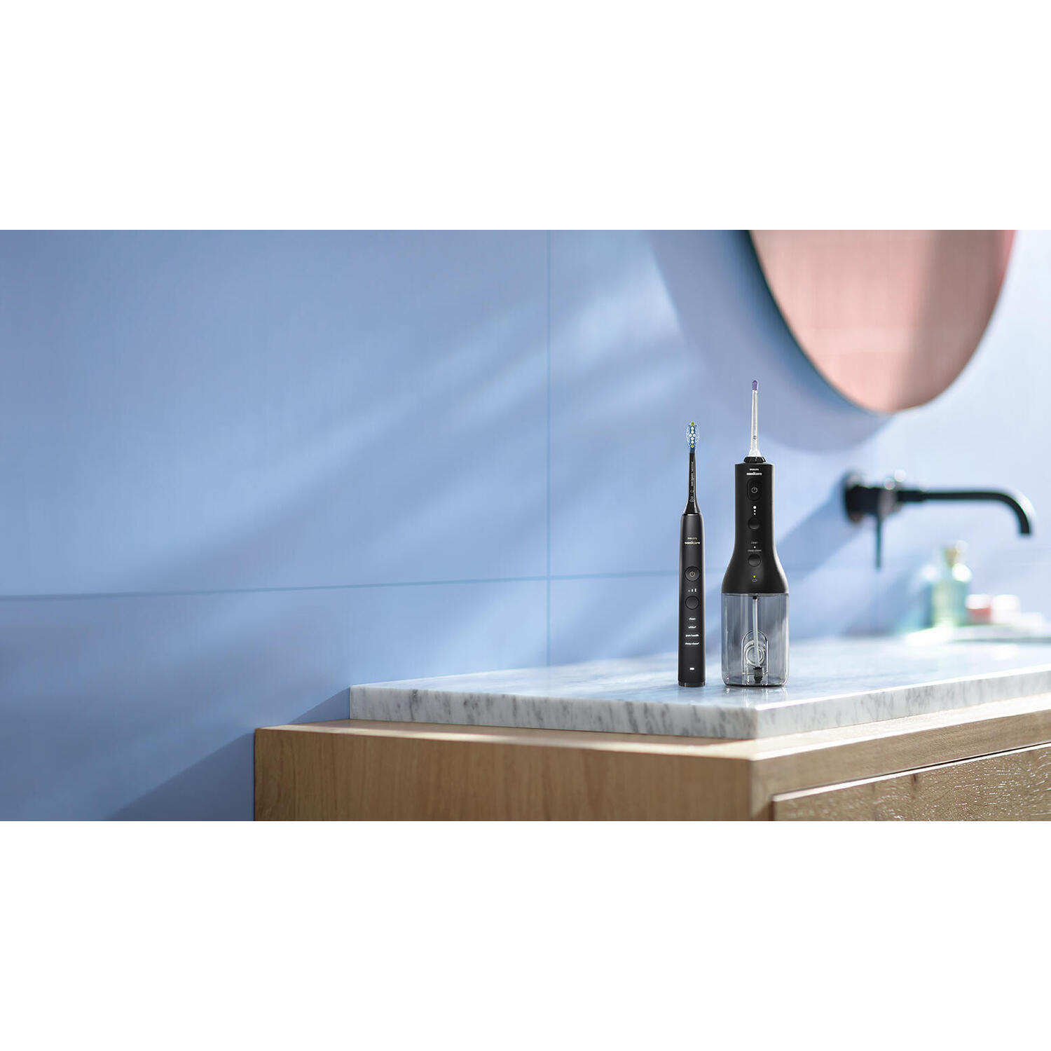 An electric toothbrush and water flosser set on a marble surface against a blue wall.