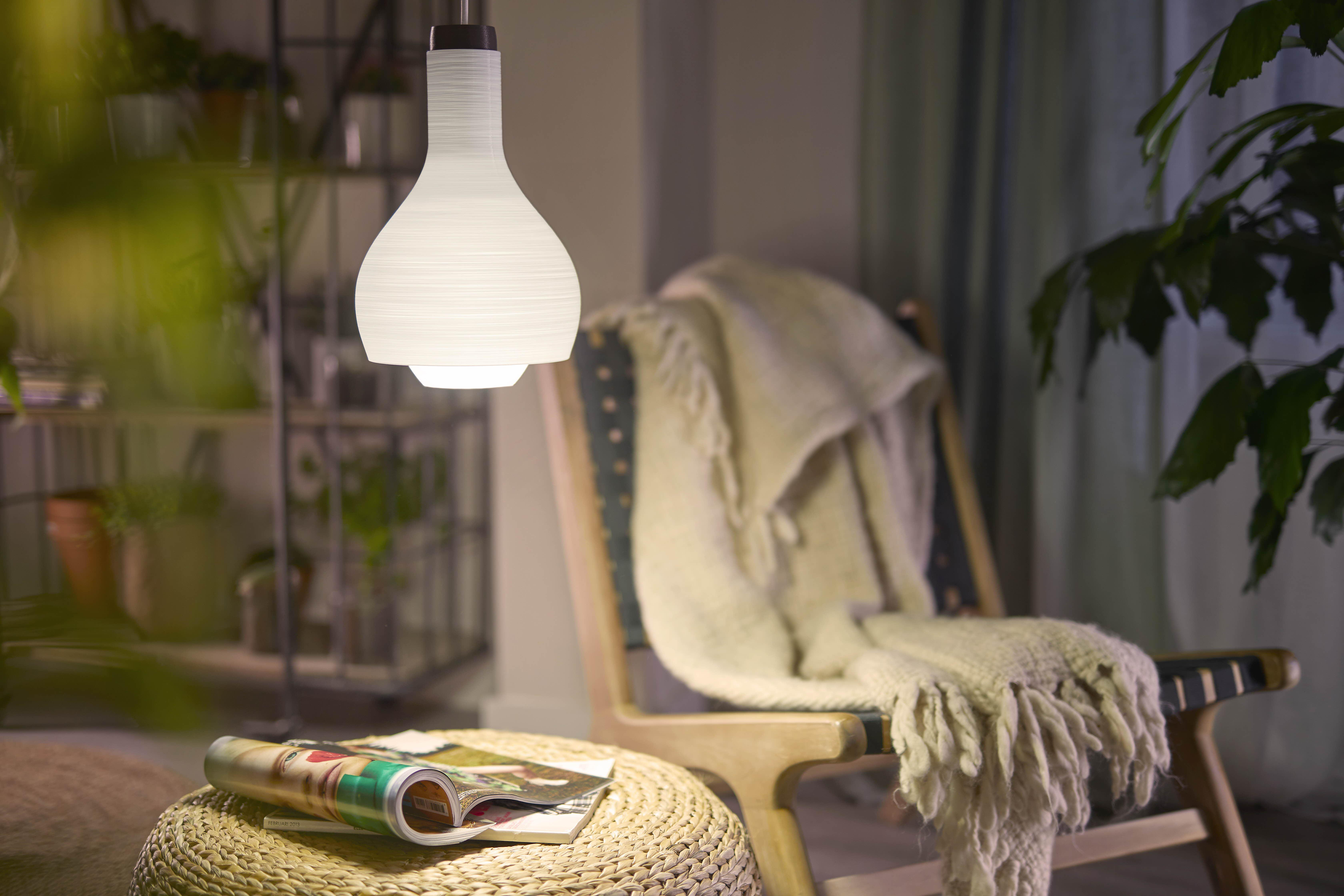Eine Lampe hängt in einem Raum mit Stuhl und Beistelltisch. Eine Zeitschrift liegt auf dem Tisch.