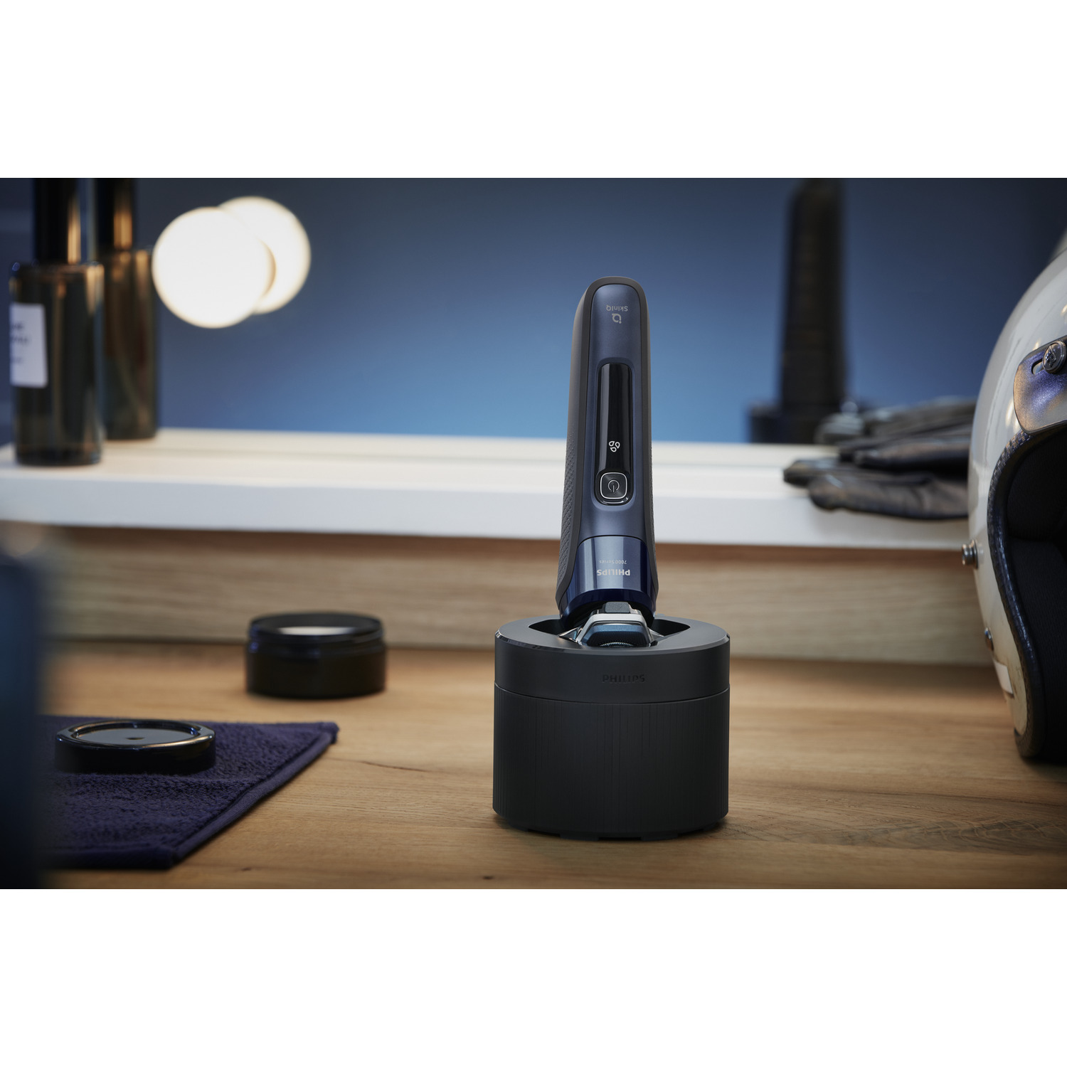 A black electric shaver on a charging stand on a wooden surface, with grooming products and a mirror.