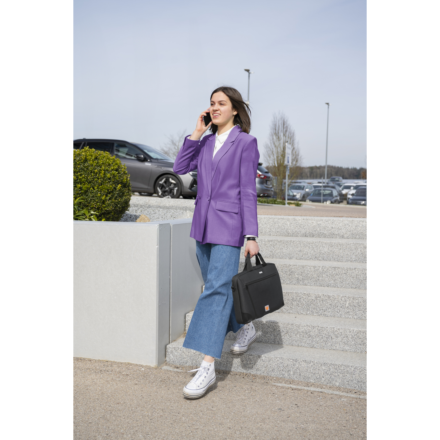 Vrouw loopt trap af, houdt tas vast, belt, buiten.