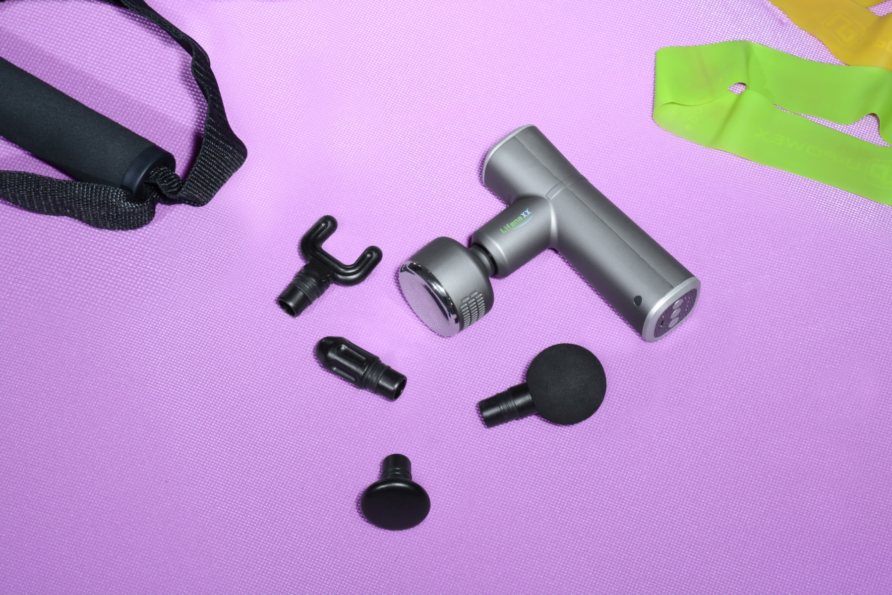 Pistolet do masażu z nasadkami i taśmami do ćwiczeń na fioletowej powierzchni.