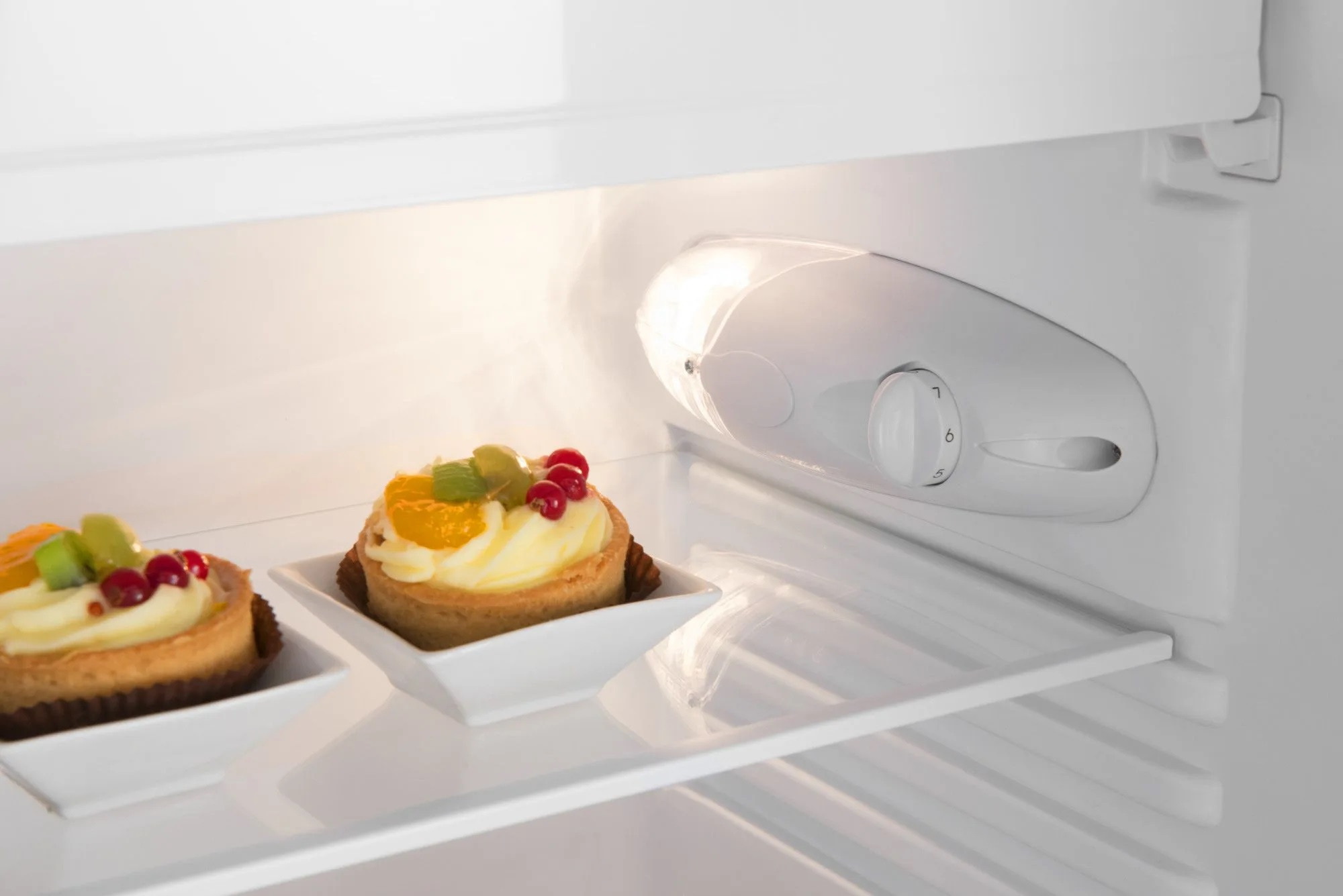 Wnętrze lodówki. Dwa tarty owocowe w białych naczyniach, światło, pokrętło temperatury.